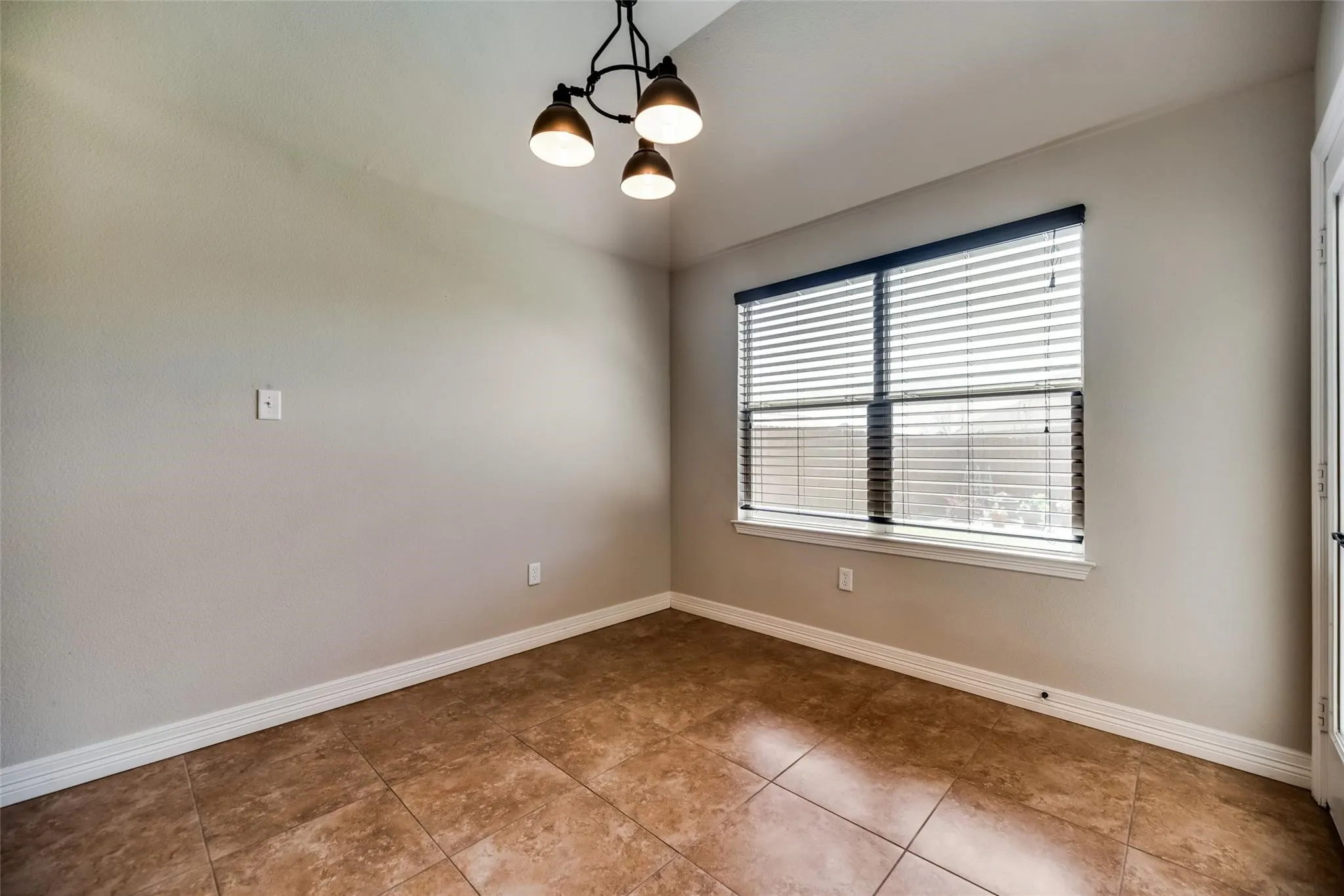 Neutral wall paint, vaulted ceiling, three-light chandelier, large window with blinds, and tile flooring