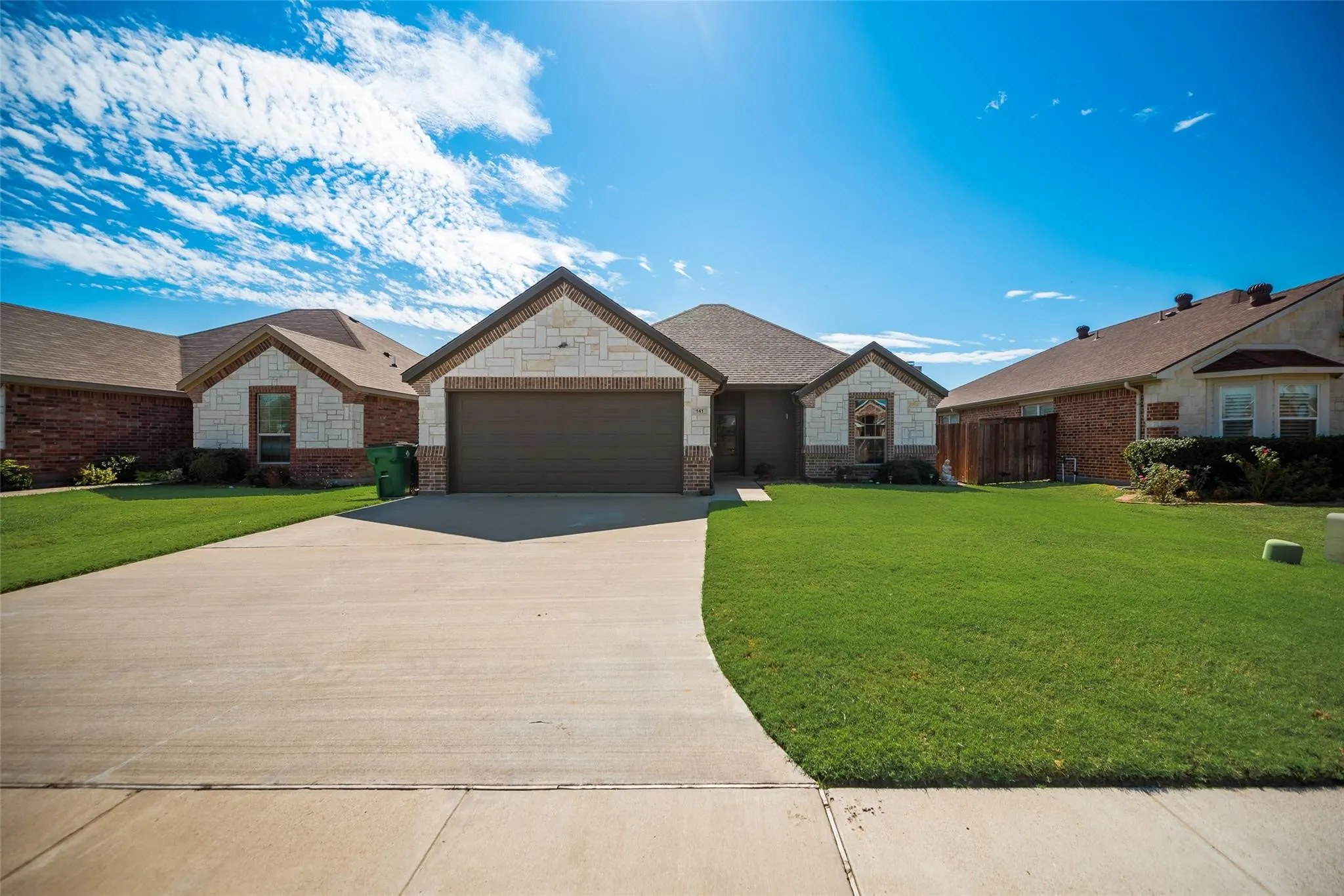 Exterior featuring a prominent attached garage, a combination of brick and stone facade, a concrete driveway, and an expansive lawn