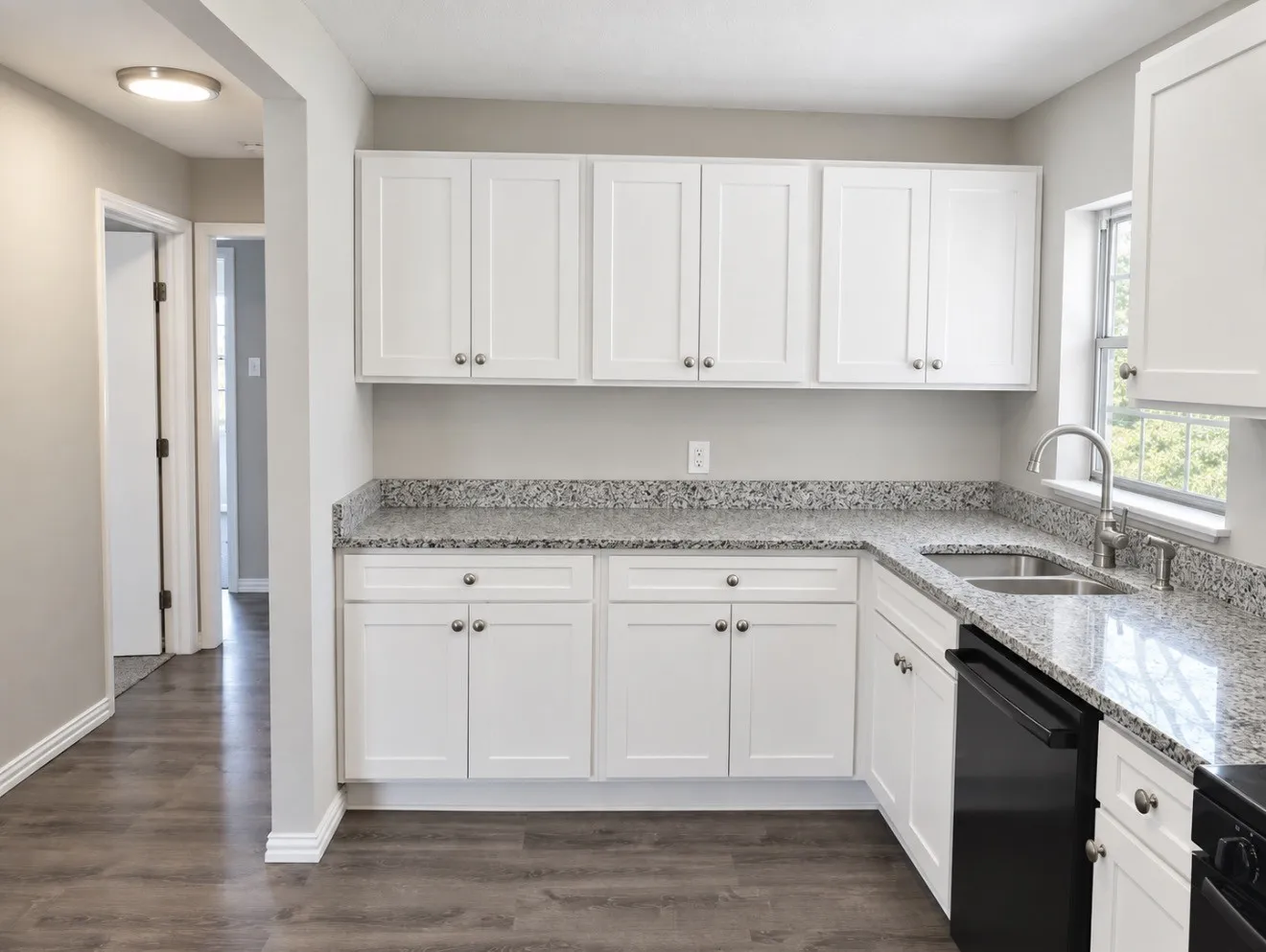 White shaker-style cabinetry, granite-style countertops, stainless steel undermount sink, and wood-finish flooring