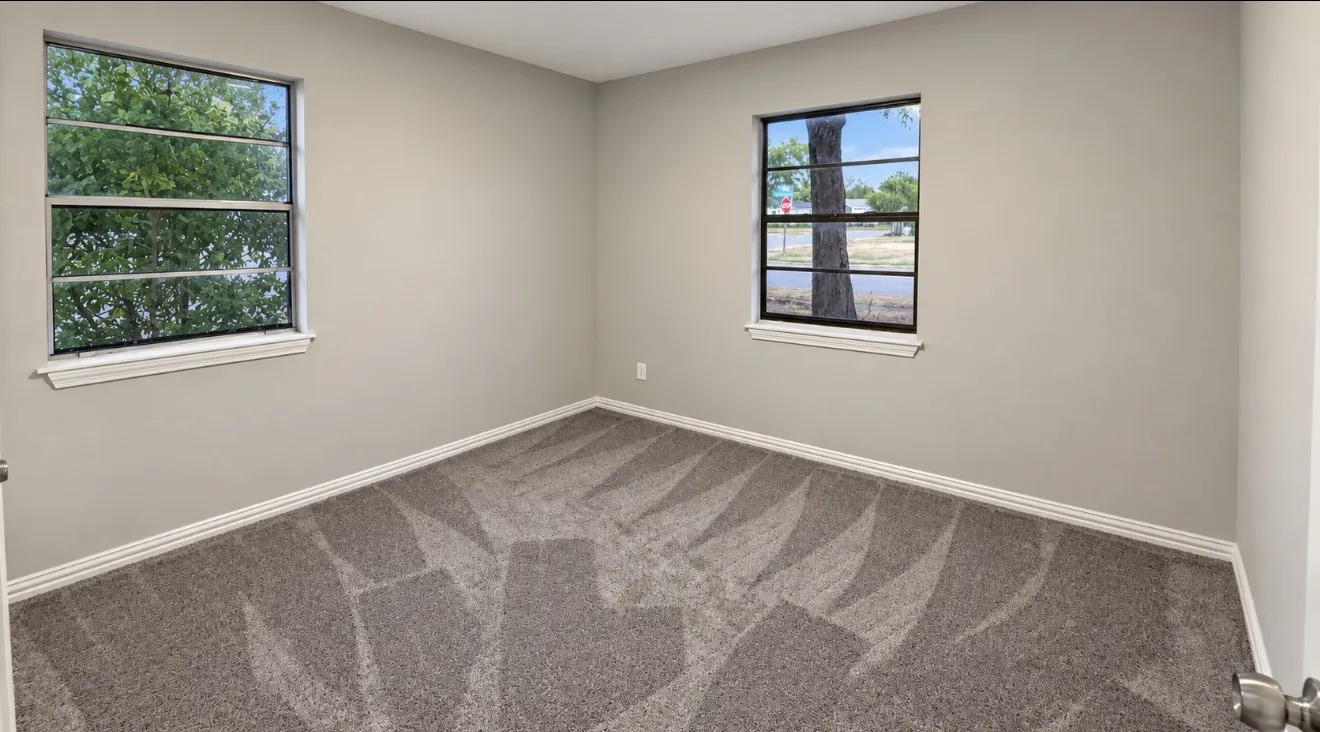 Neutral wall paint, patterned carpeting, two windows, and white trim molding