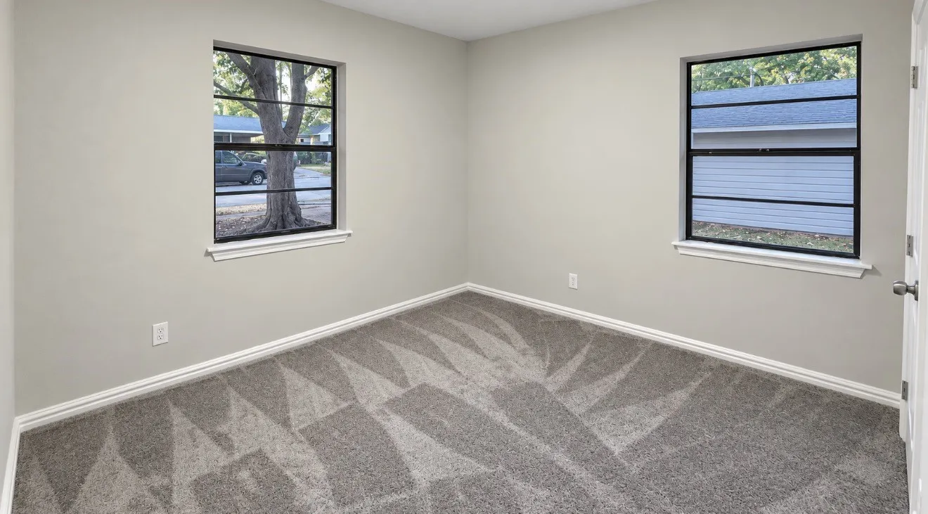 Neutral wall paint, patterned carpeting, two windows with black frames, and white trim throughout