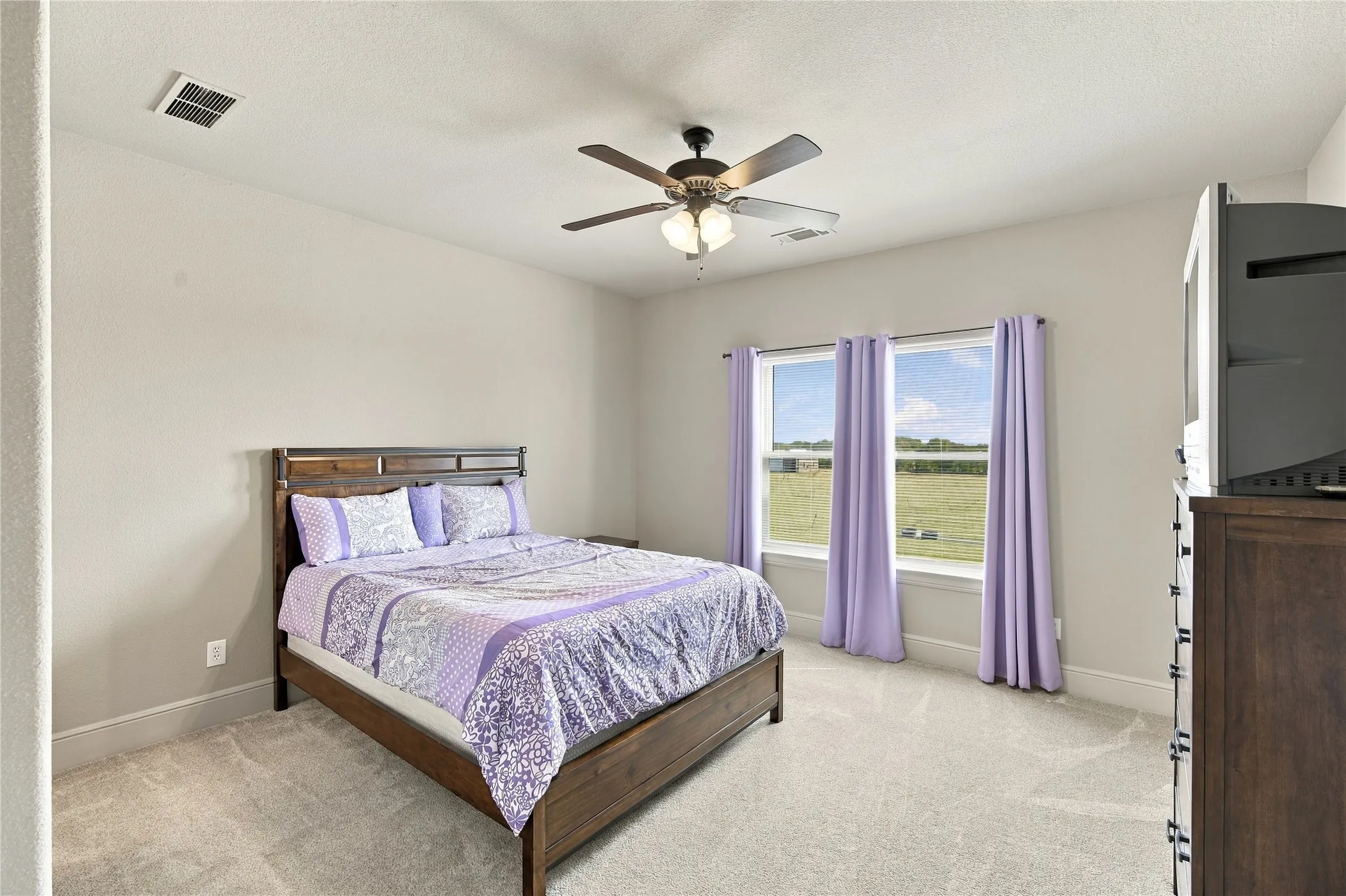 Neutral wall tones and dual windows give this bedroom a calm, versatile feel, ideal as a guest room, home office, or nursery.