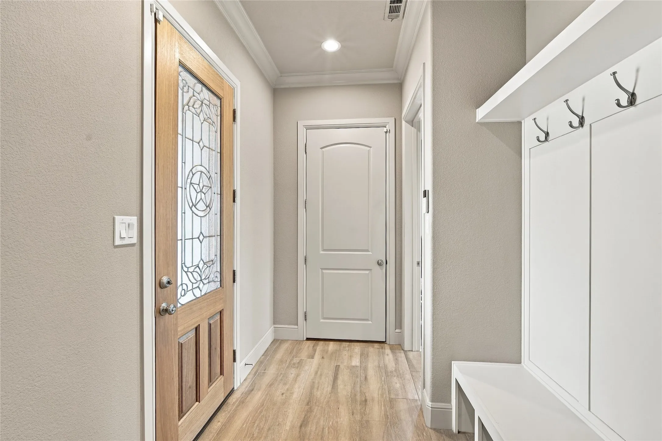 A stylish drop zone with a leaded-glass door, crown molding, tile flooring, and a built-in bench with coat hooks, perfect for keeping busy mornings organized.