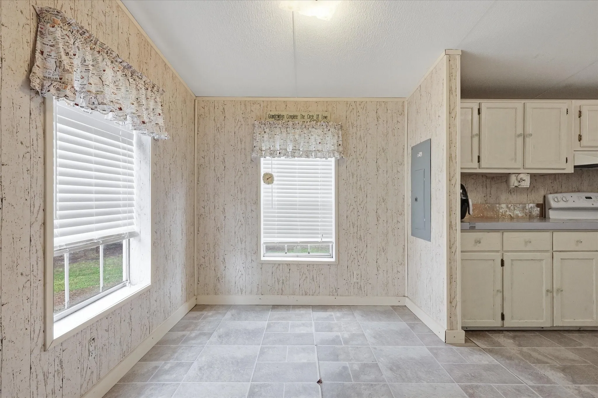 Light-toned tile flooring, two windows with horizontal blinds, built-in upper and lower cabinetry, and a light-toned countertop