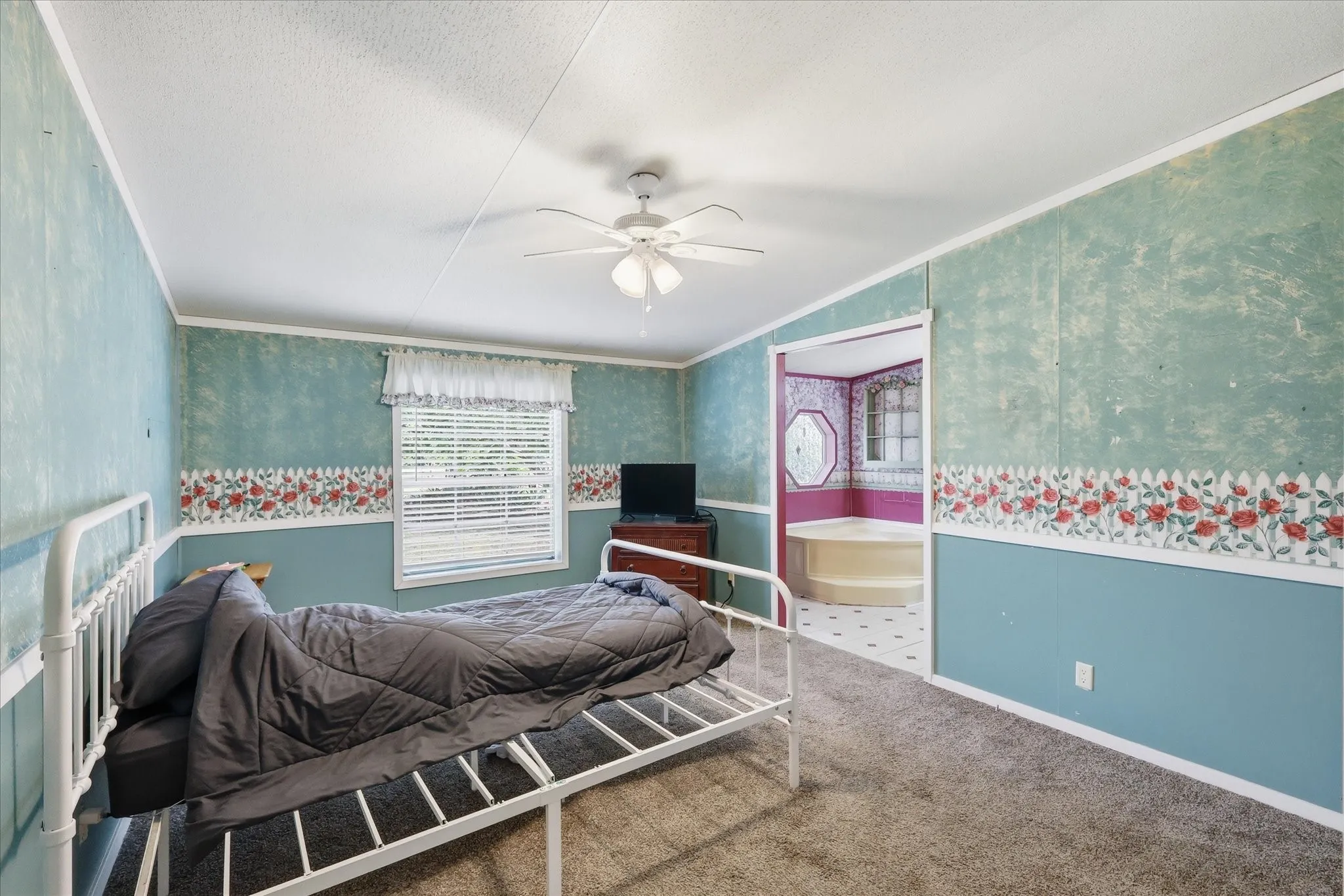 Carpeted room featuring a ceiling fan, window with blinds, and an entryway to an adjoining space with a built-in tub