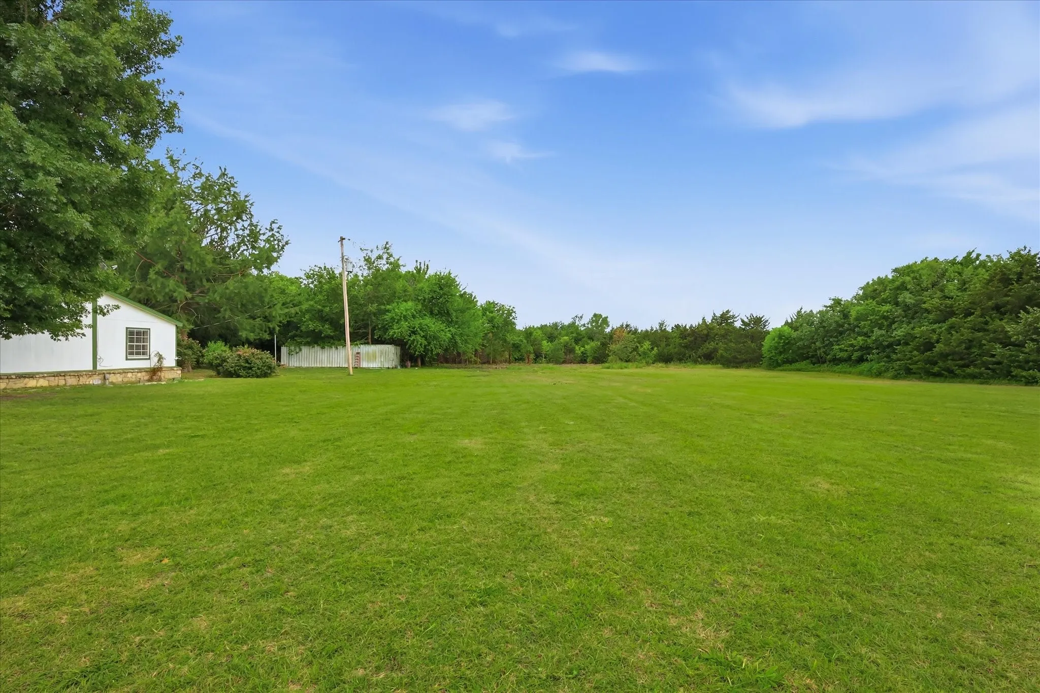 Expansive green lawn surrounded by mature trees, featuring a white structure with a dark-framed window