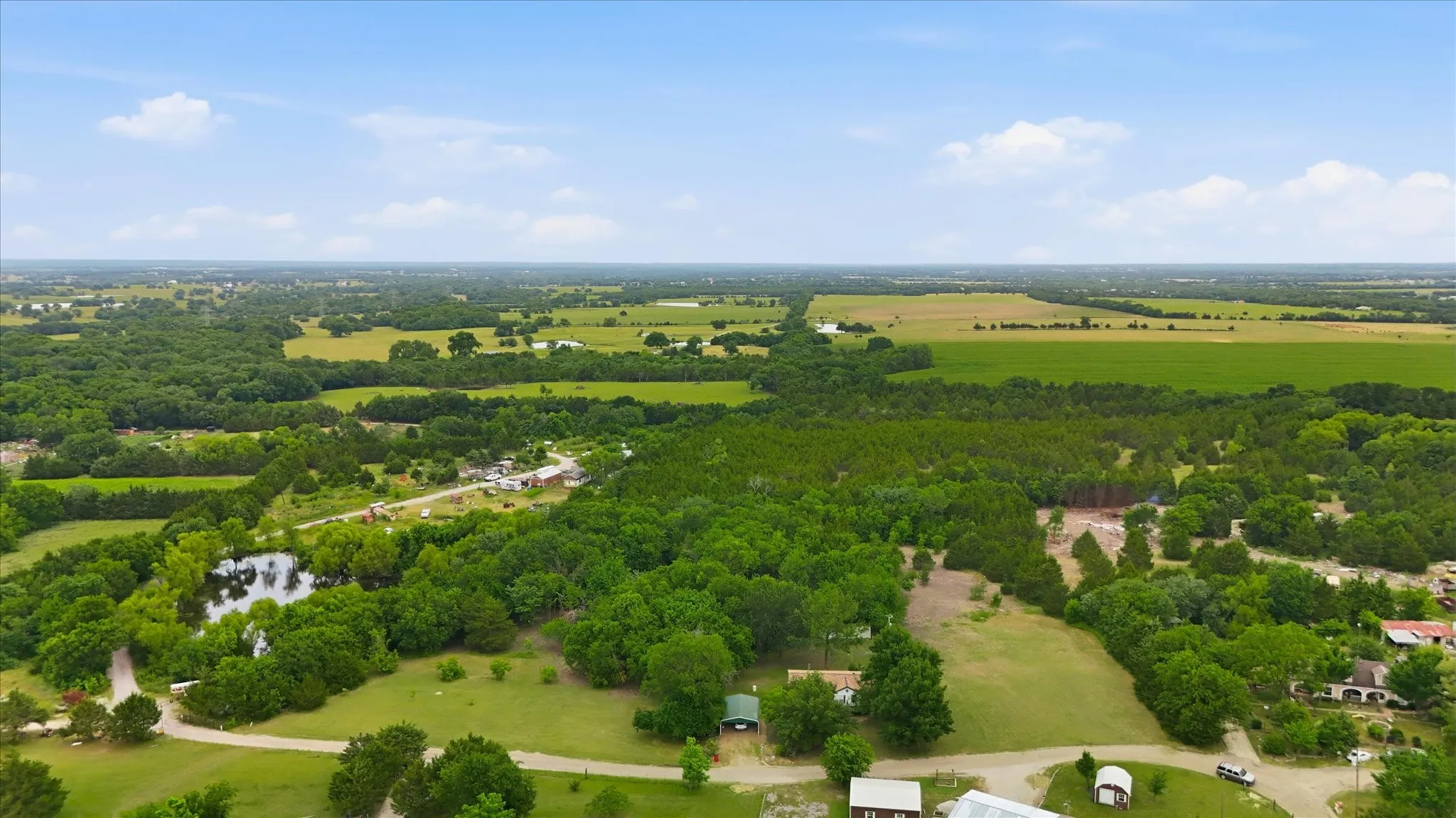 Expansive rural landscape featuring a natural pond, diverse tree cover, open fields, and residential structures