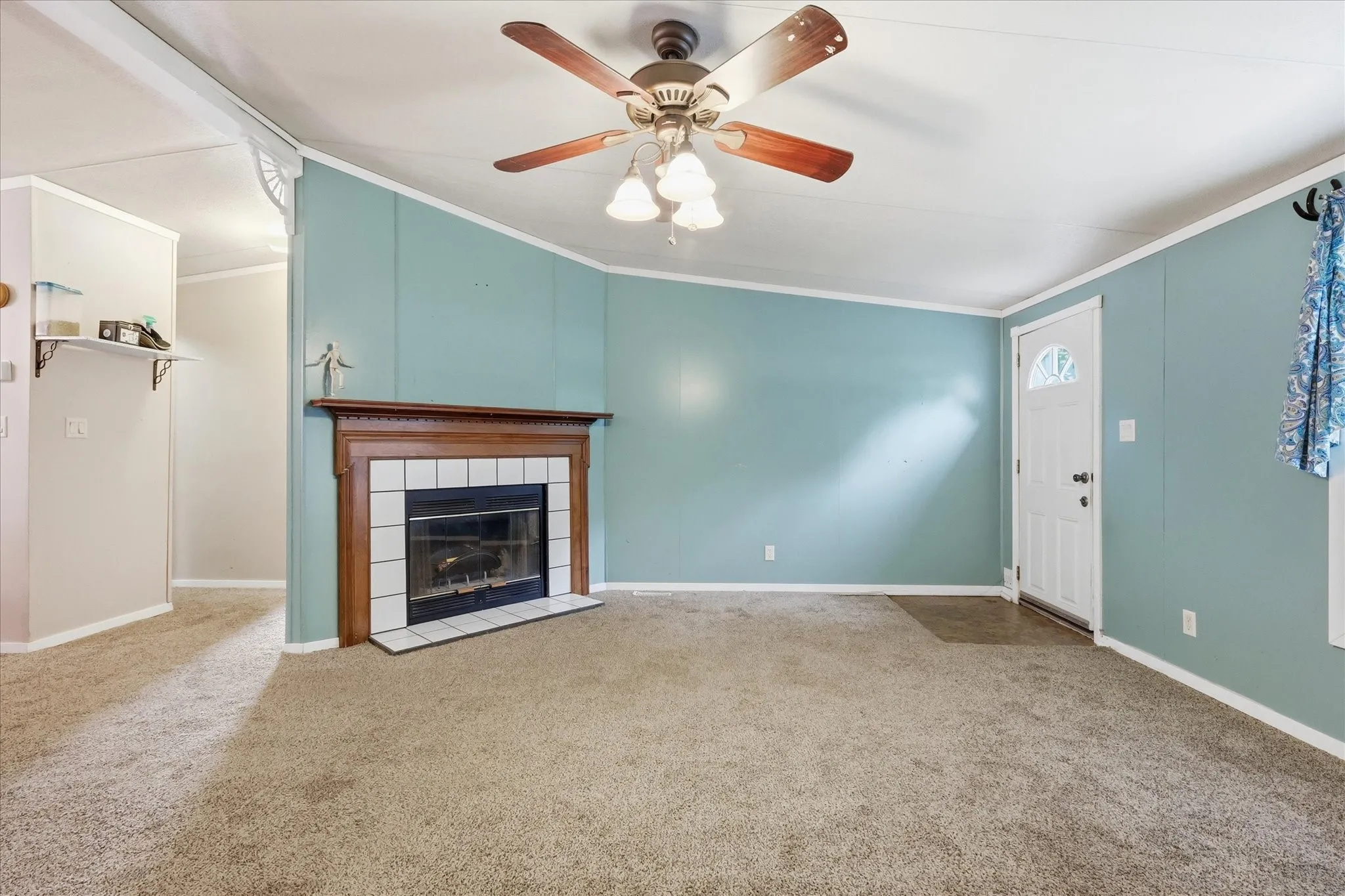 Living area featuring carpeting, a ceiling fan, a fireplace with a wood mantel and tile surround, and a white entry door with a decorative glass insert