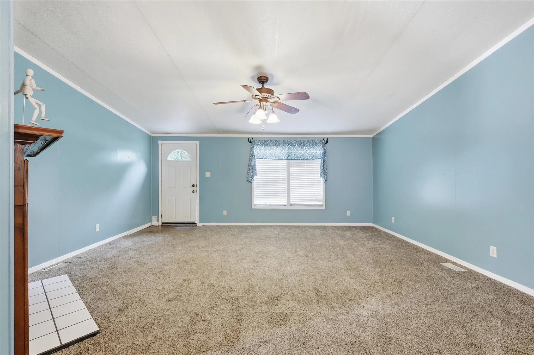 Spacious room with light blue walls, carpeted flooring, a ceiling fan with integrated lighting, and a white entry door with an arched window