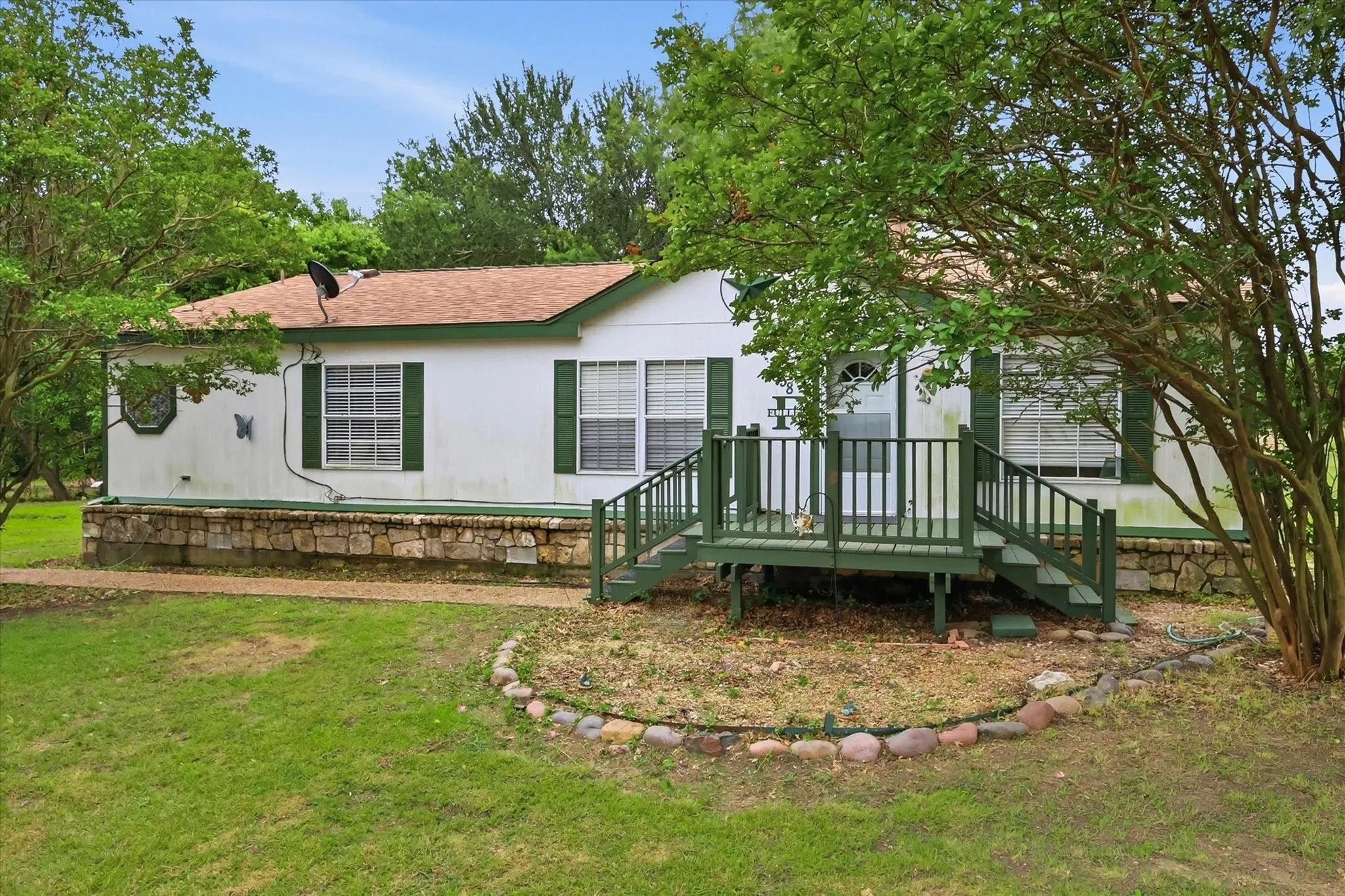 White exterior with green shutters, a front porch with railing, and a stone foundation