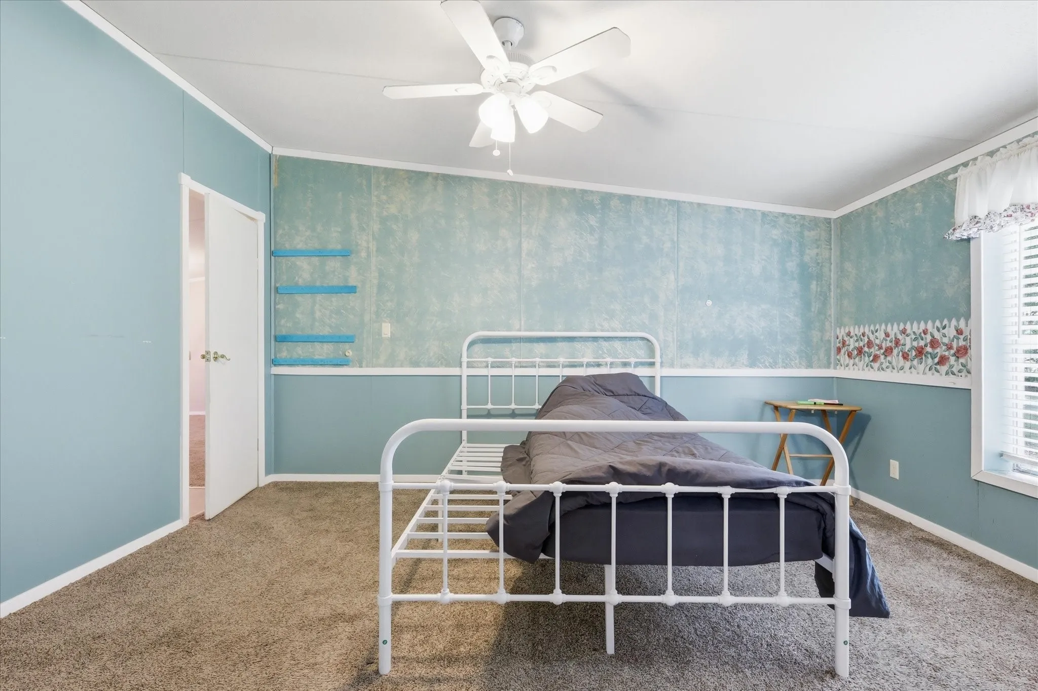 Carpeted flooring, ceiling fan with light fixture, window with blinds, interior door, and wall-mounted shelving