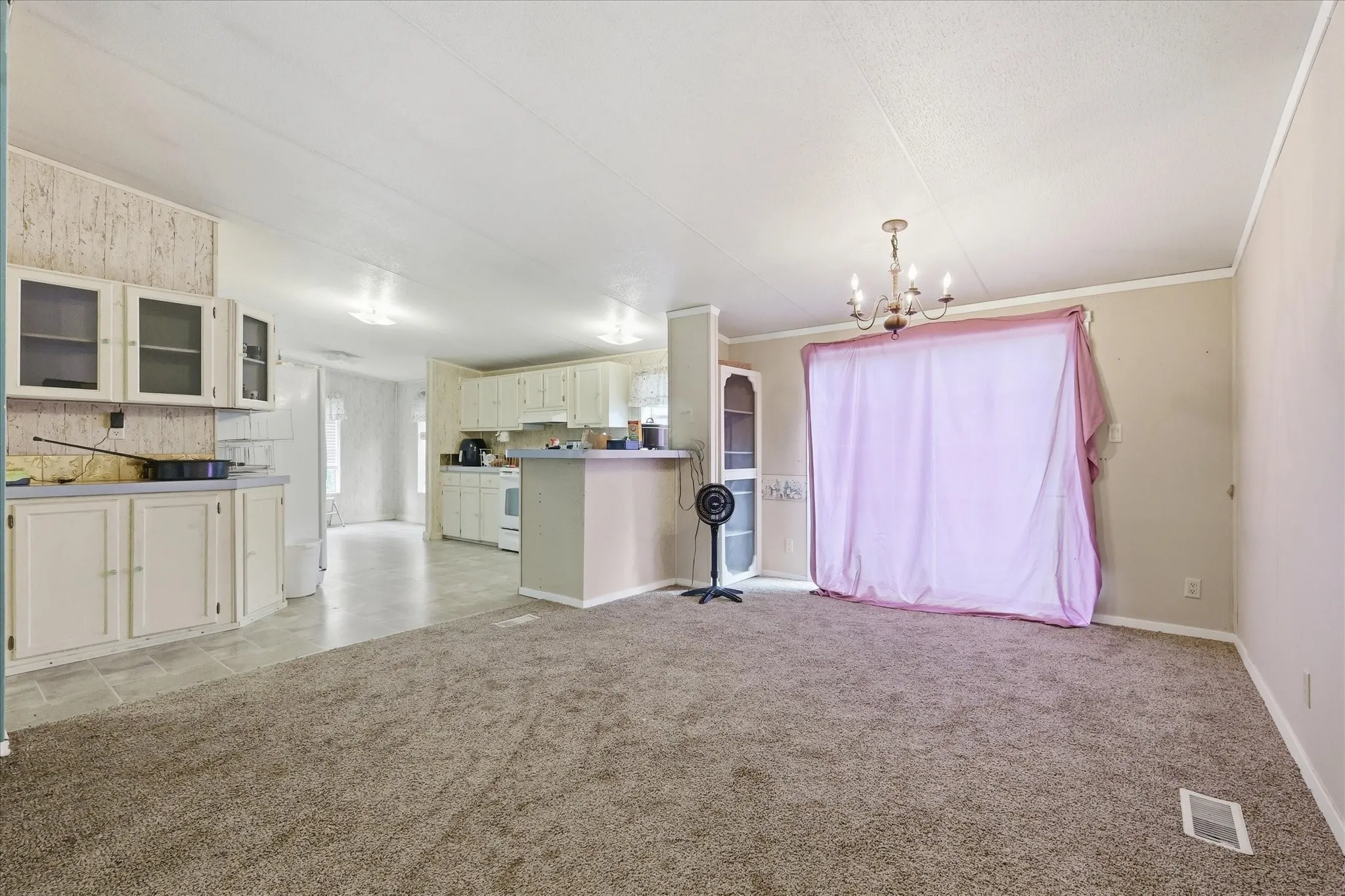 Open concept living area featuring carpet flooring, a multi-light chandelier, and an integrated kitchen with ample cabinetry