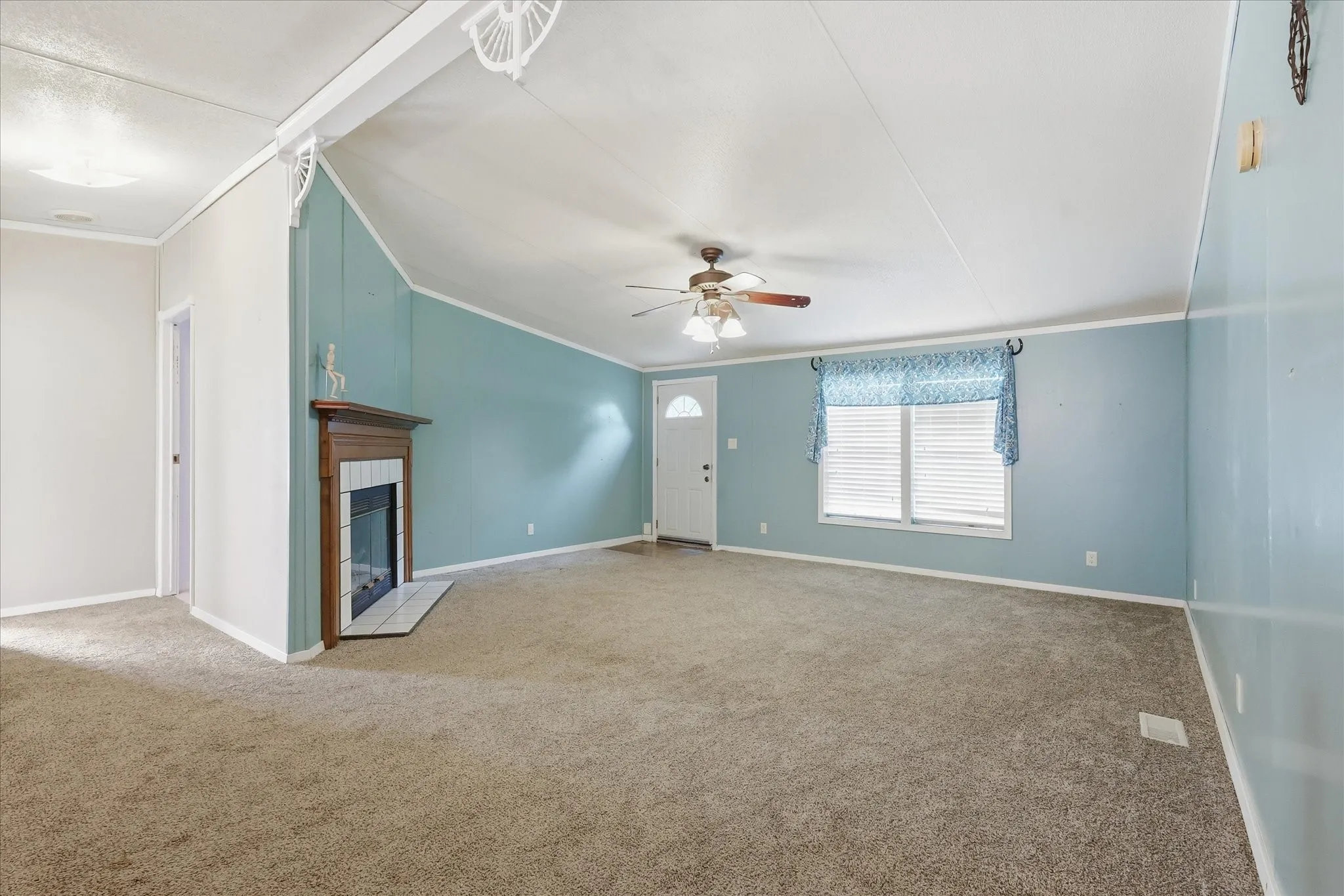 Carpeted living space with a wood-mantel fireplace, ceiling fan, and a front entry door with a frosted glass insert