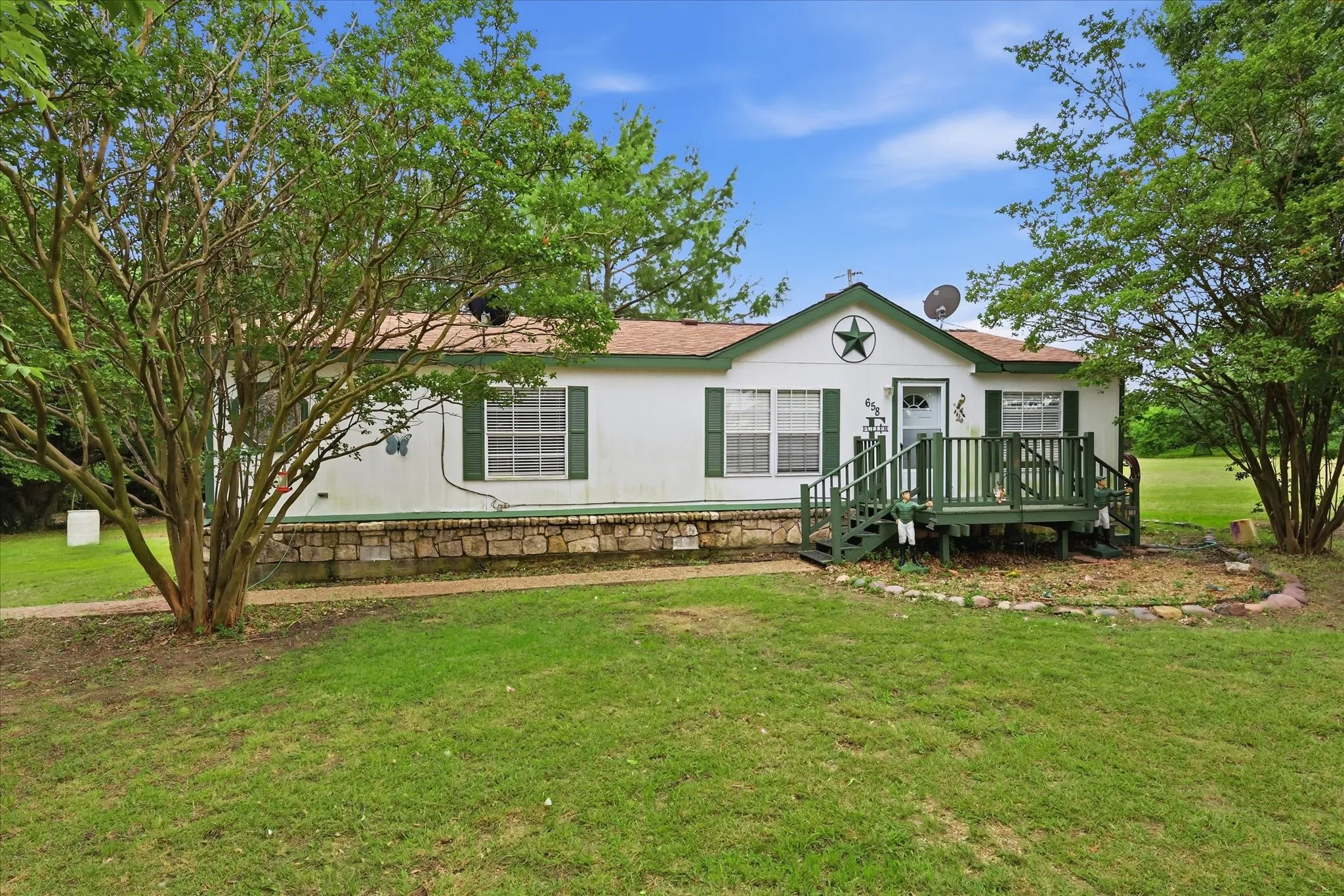 White exterior with green shutters and trim, a front deck with railings, and a stone-look foundation