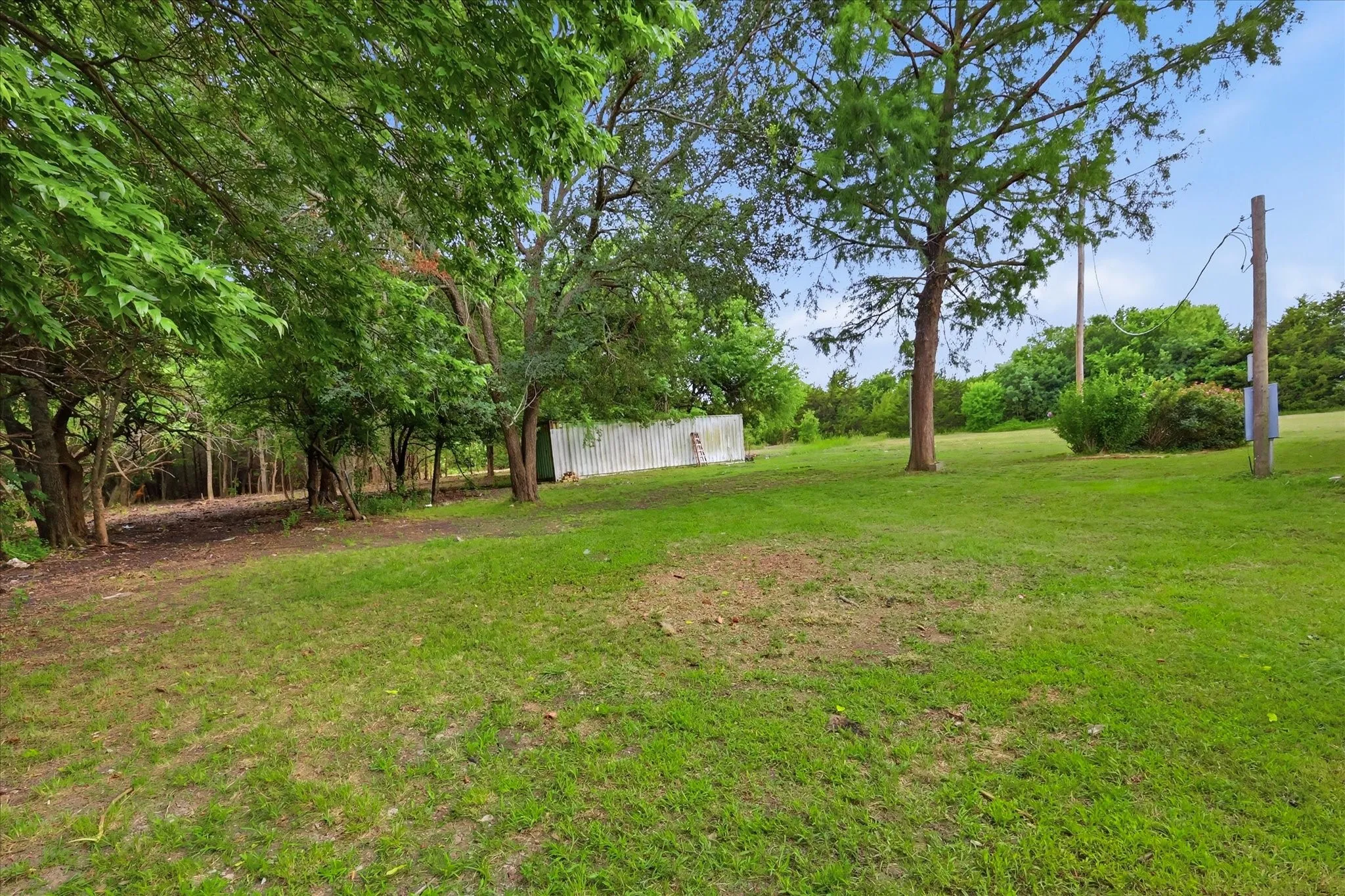 Expansive open lot featuring mature trees and a partial privacy fence