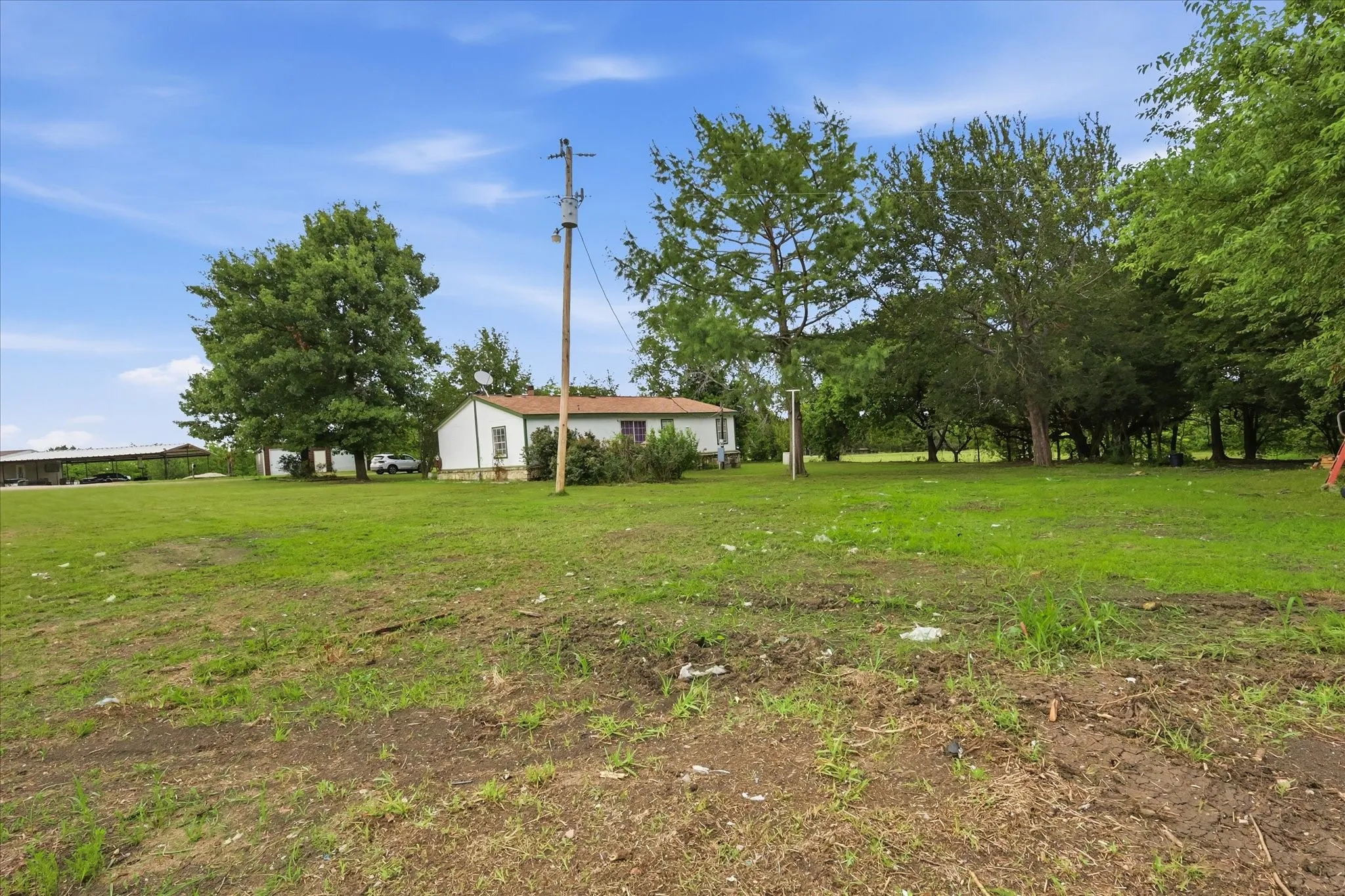 Expansive green lawn with mature trees and a residential structure