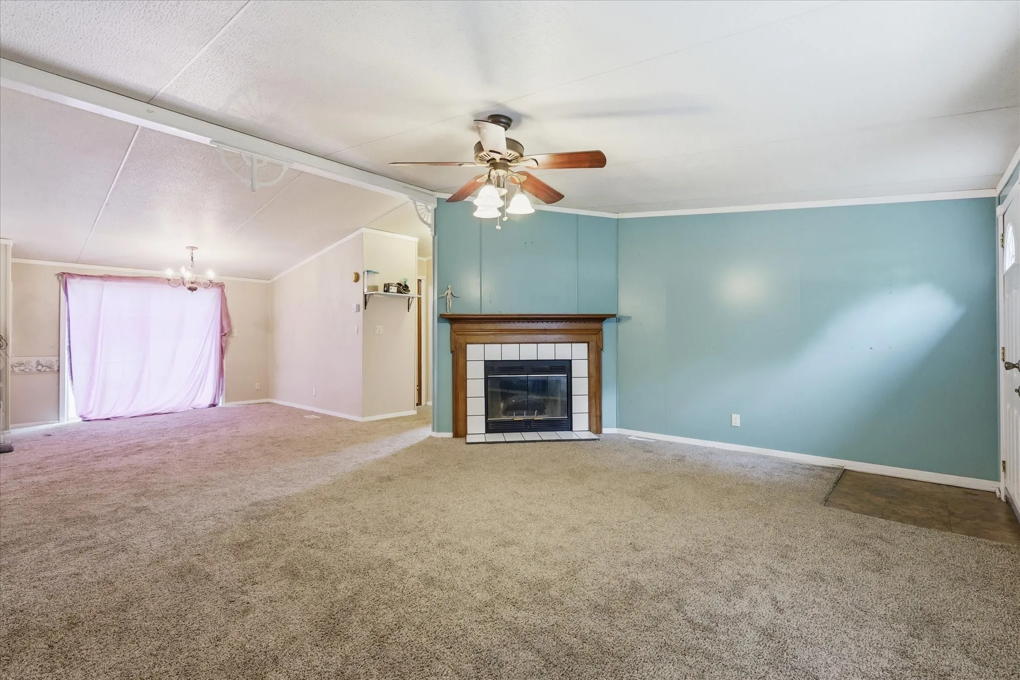 Carpeted living space featuring a fireplace with a wood-finish mantle and white tile surround, a ceiling fan, and a chandelier in the dining area