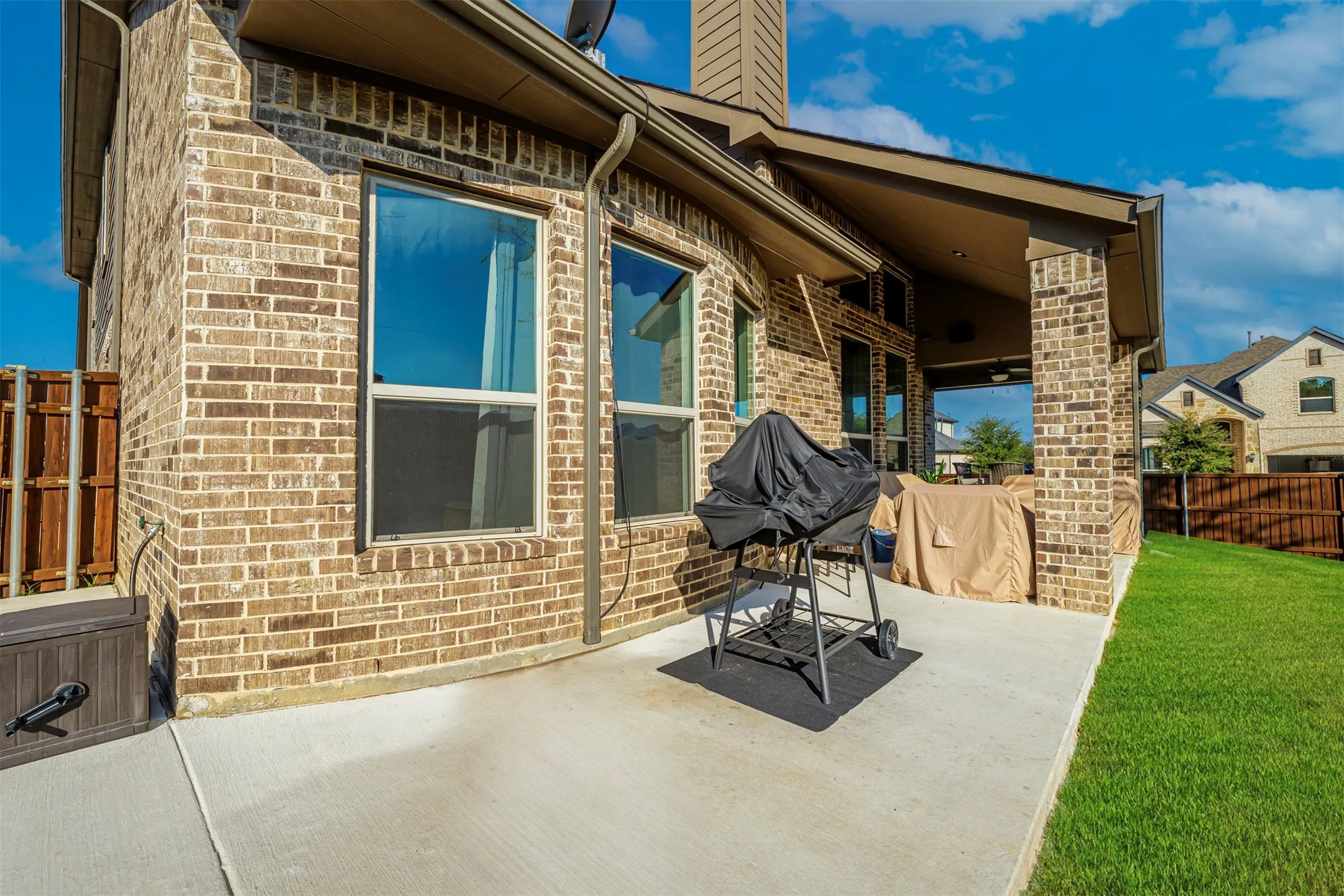 Brick exterior with multiple windows, concrete patio, covered outdoor living space, and a manicured lawn
