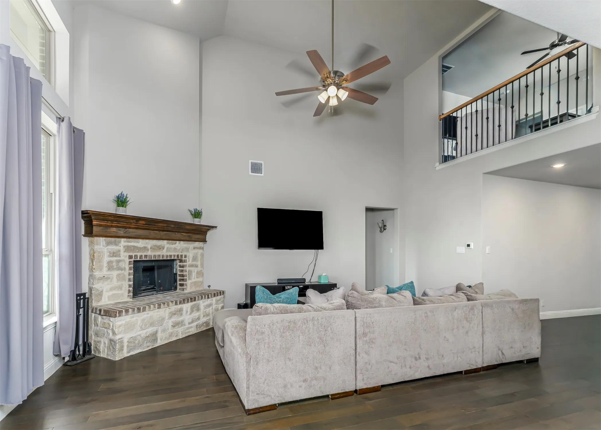 Two-story living area with a stone fireplace, wood-finish flooring, high ceilings, and a second-story interior balcony with black metal balusters