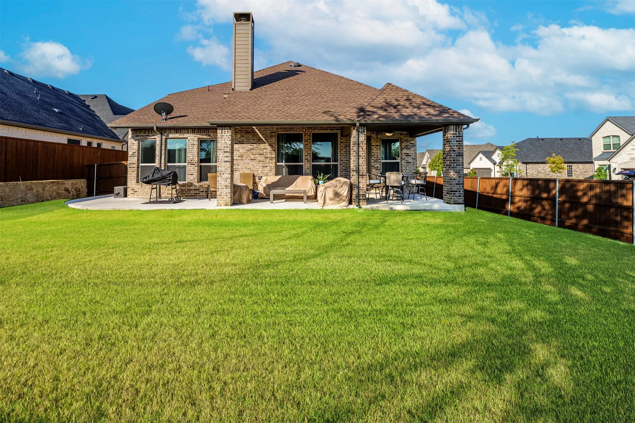 Expansive green lawn with a covered patio, brick exterior, and a privacy fence