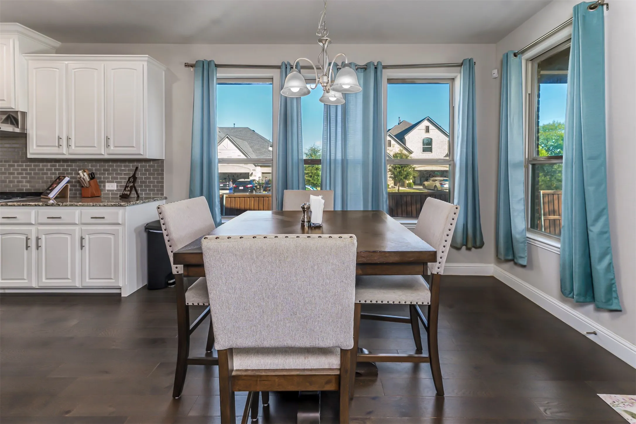 White cabinetry, tiled backsplash, wood-finish flooring, and multiple windows