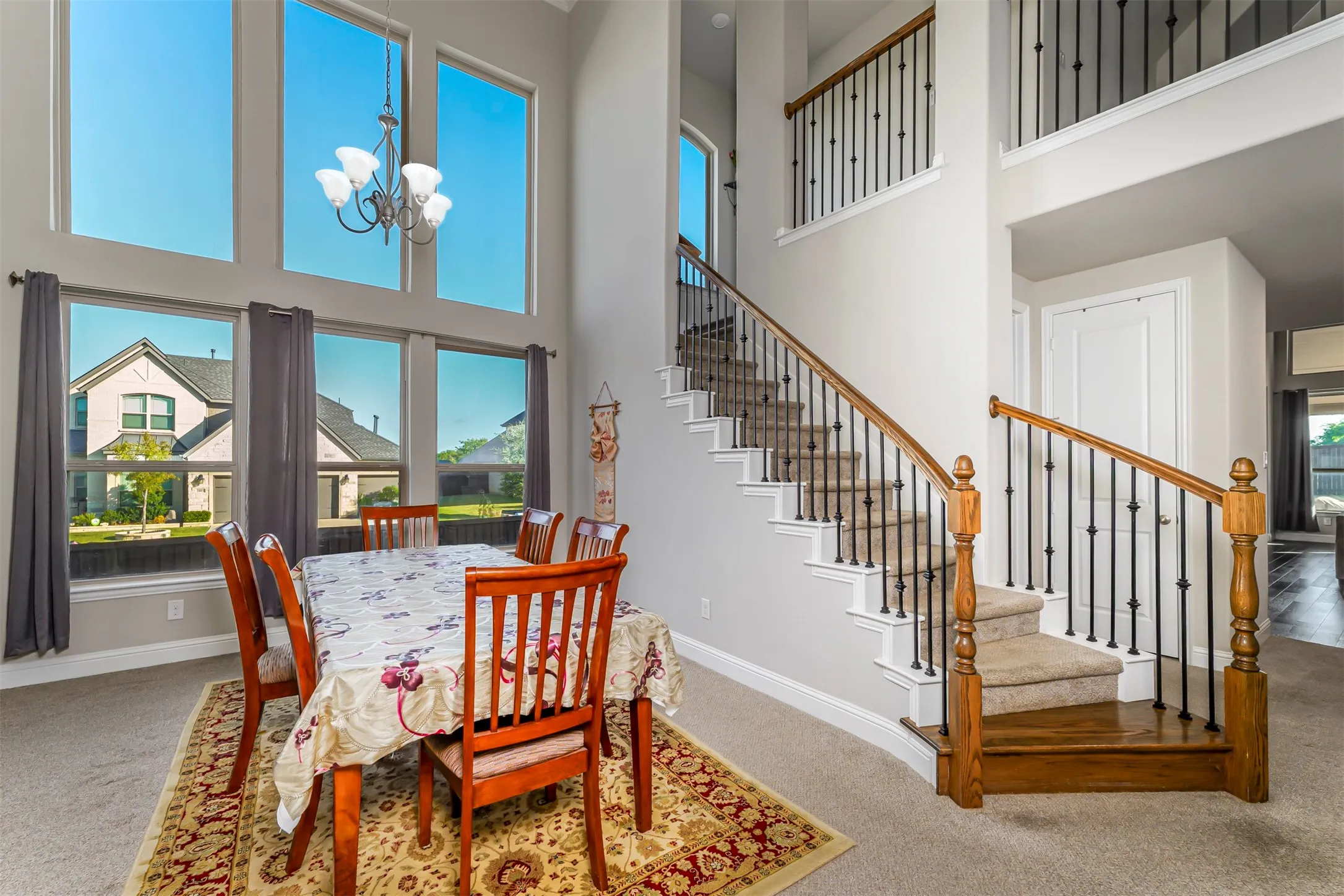 Two-story living area with a chandelier, high ceilings, large windows, and a staircase with wood handrails and wrought iron balusters