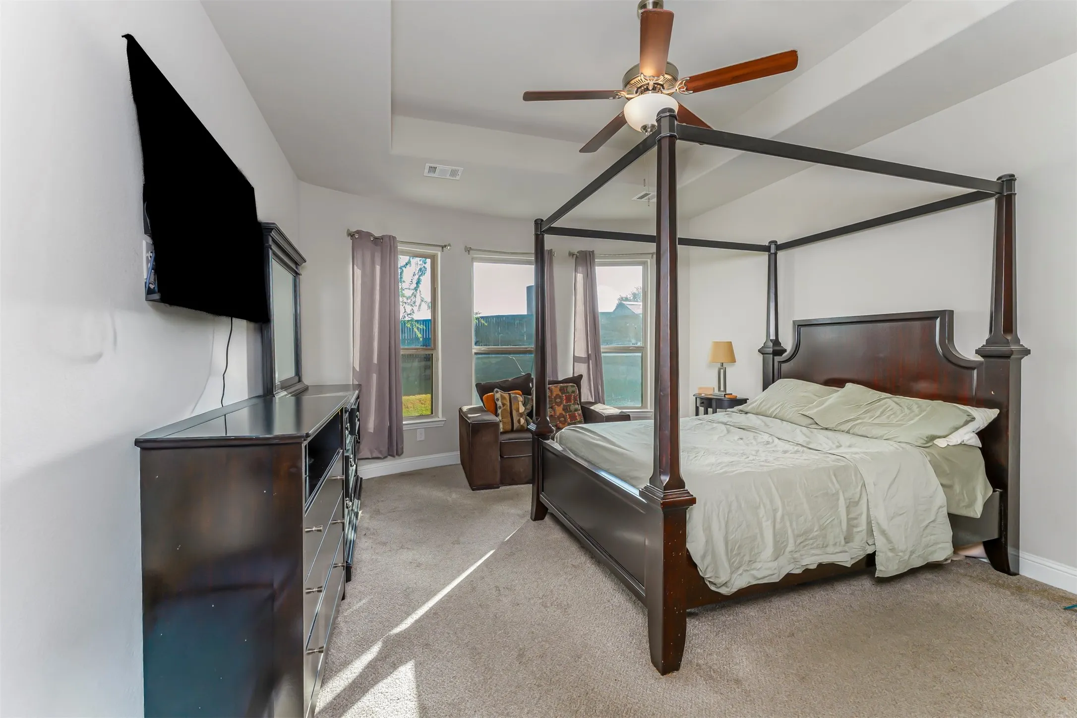 Recessed ceiling with a central fan, light gray carpeting, and multiple windows providing natural illumination