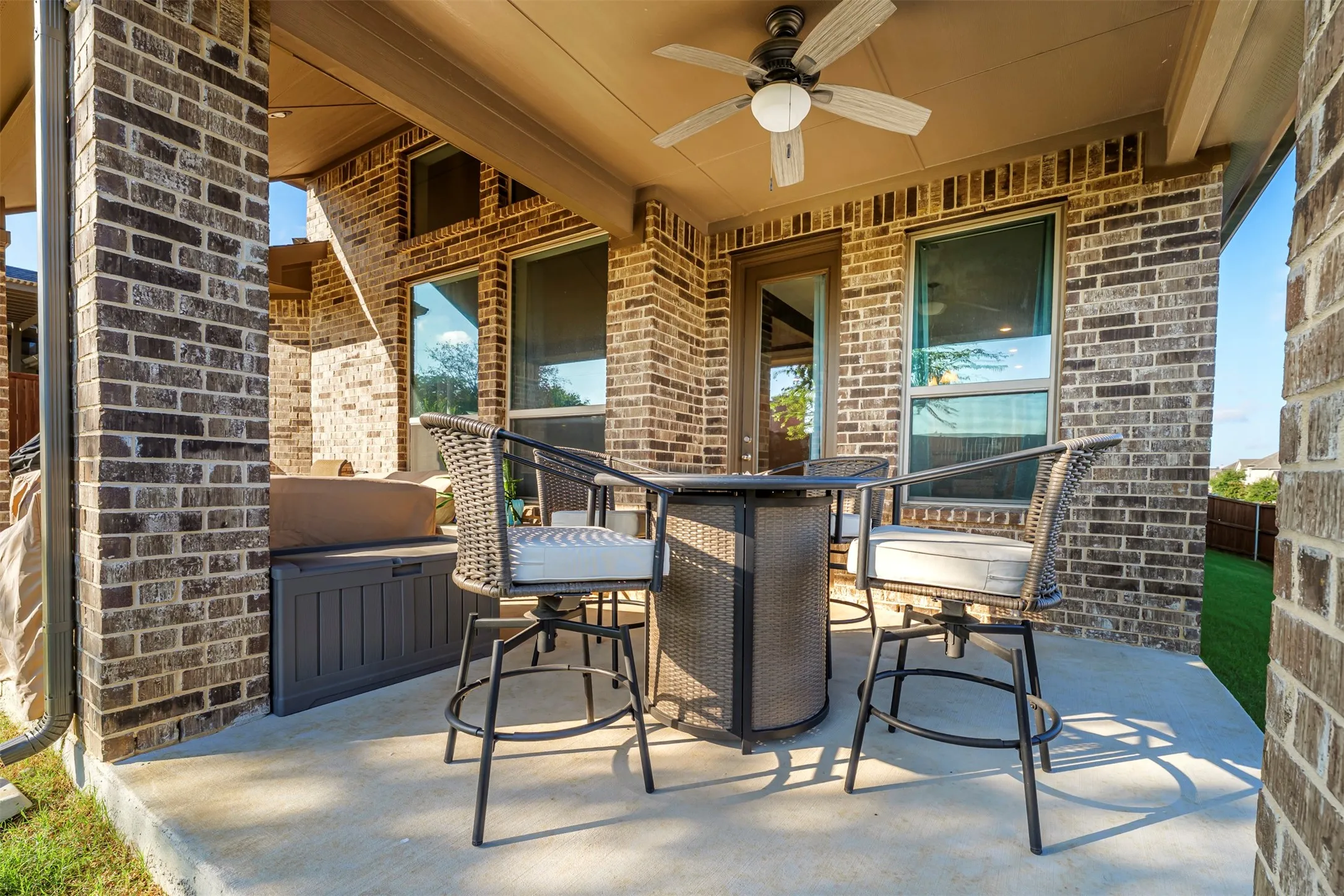 Covered patio featuring a ceiling fan, brick exterior, concrete flooring, and an exterior door