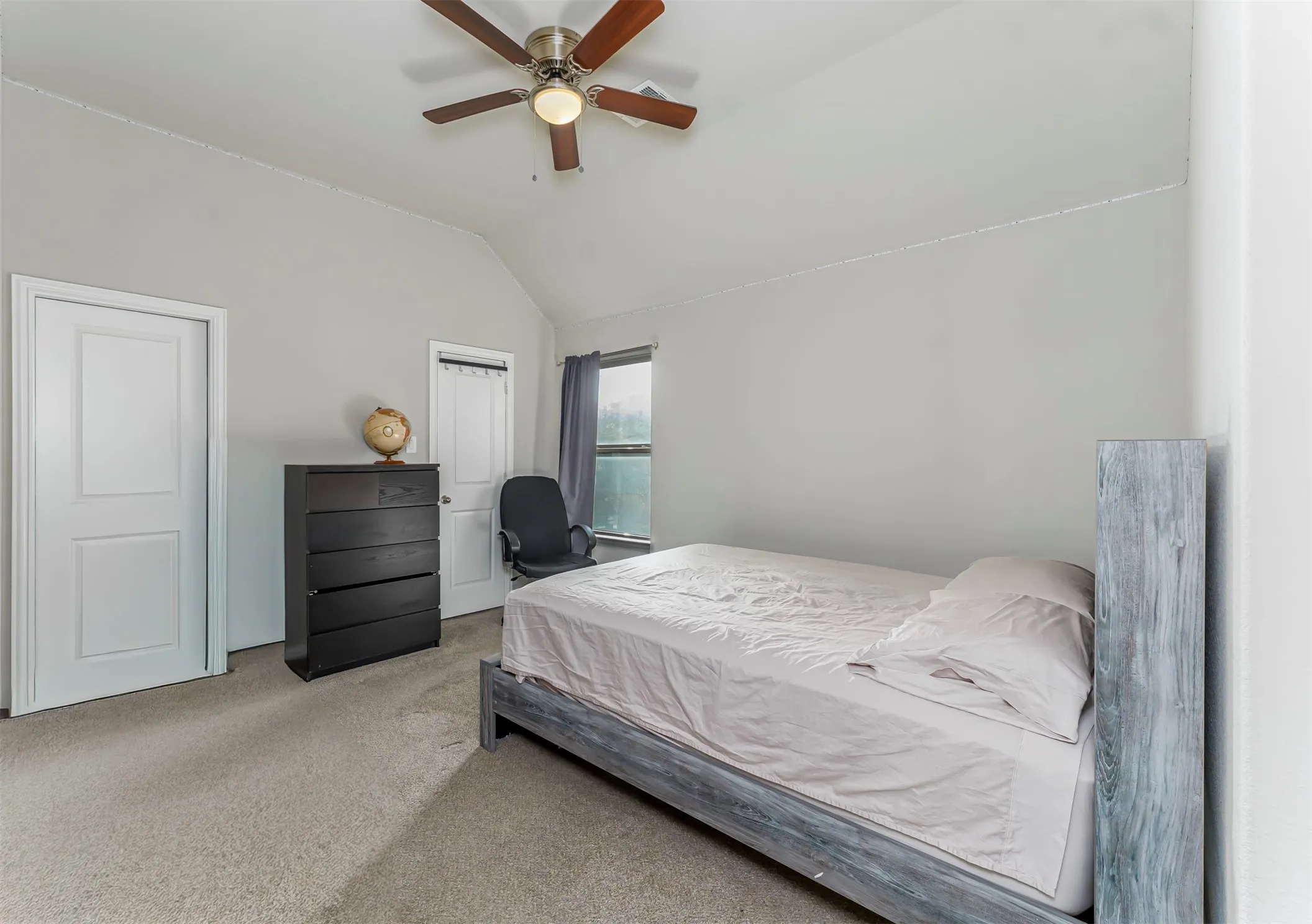 Vaulted ceiling, ceiling fan with integrated lighting, neutral-toned carpeting, two-panel interior doors, and window with dark drapes