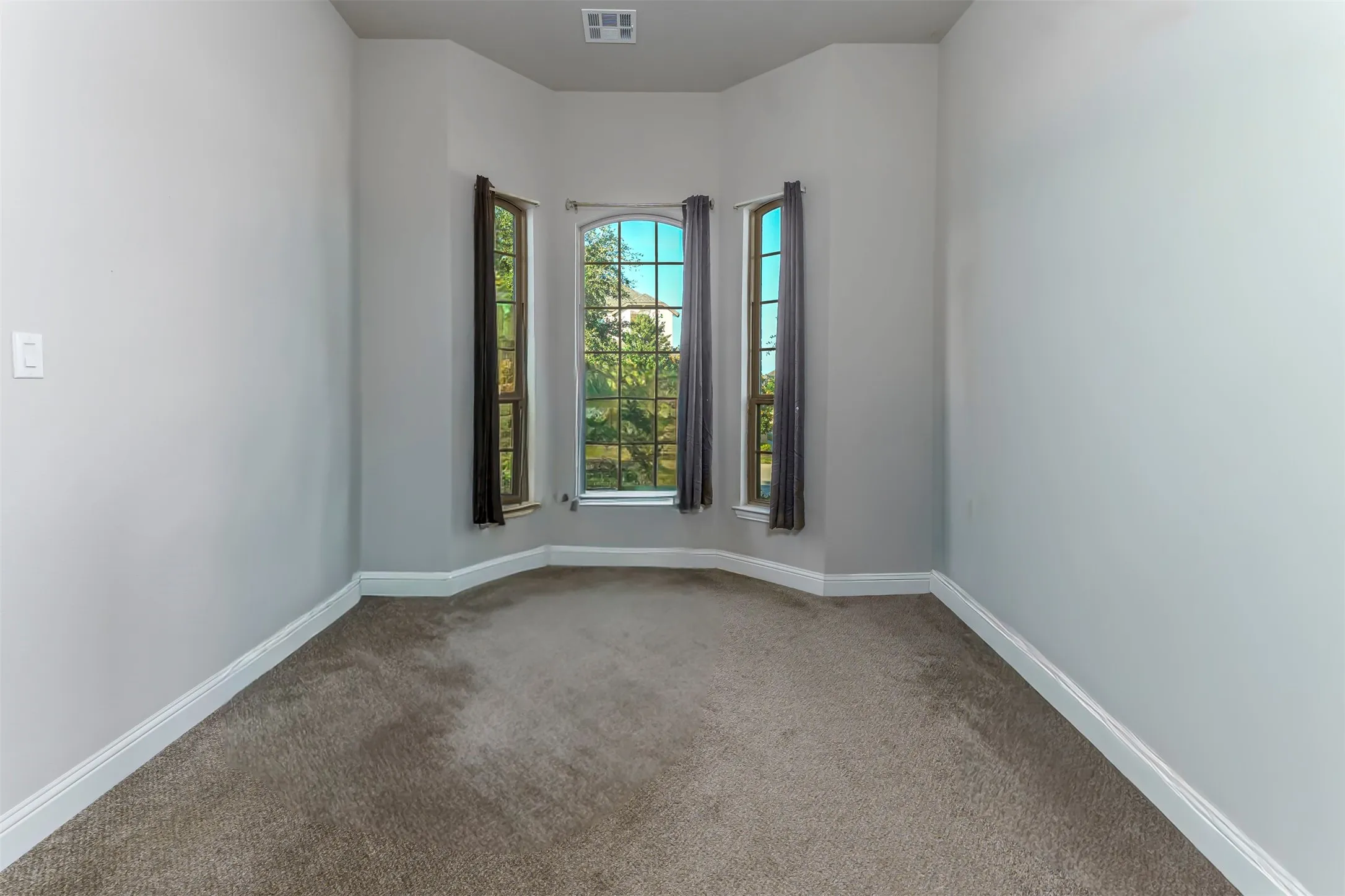 Recessed bay window with an arched central pane, gray carpeting, and white baseboards