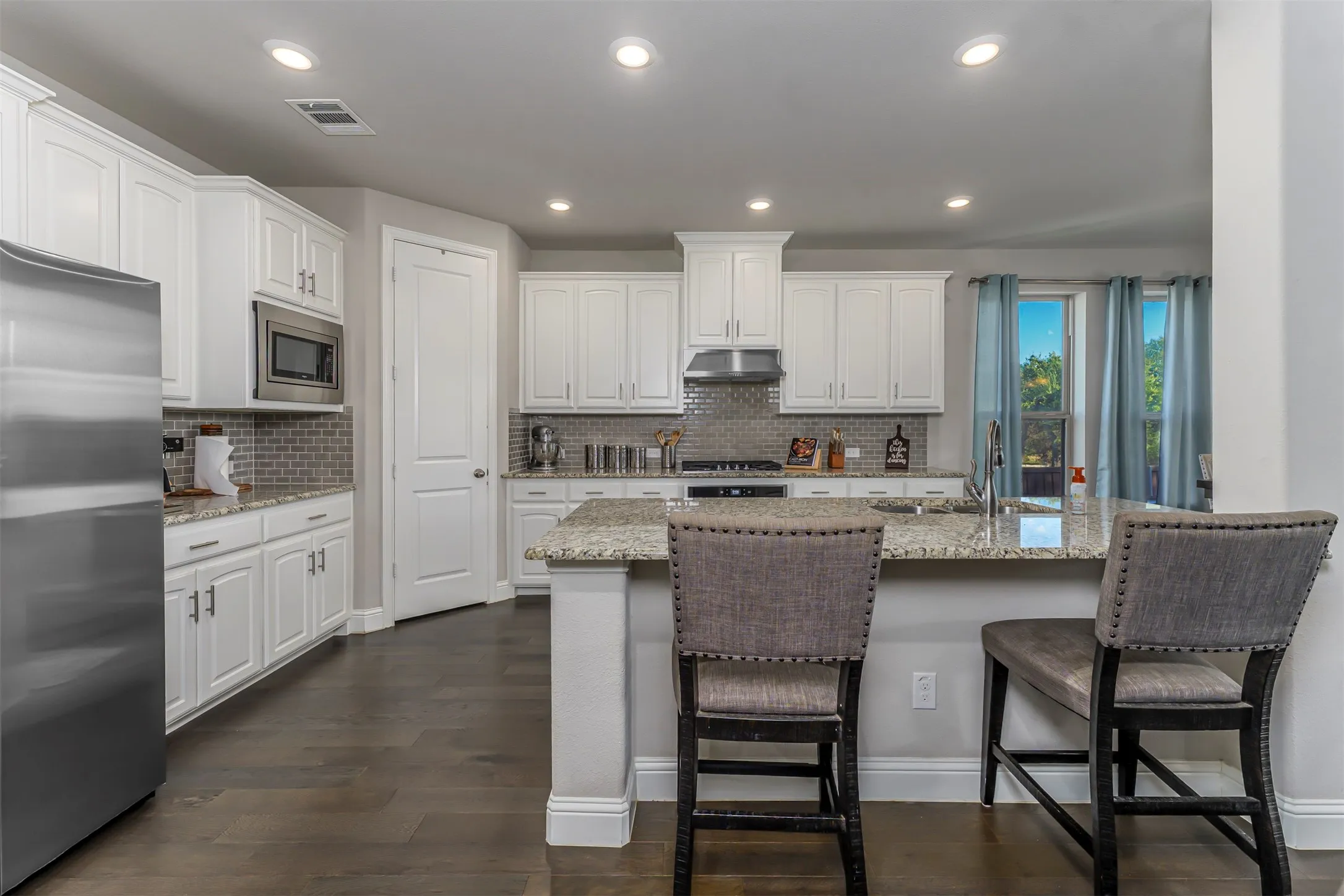 Kitchen featuring white cabinetry, stainless steel appliances, granite countertops, tile backsplash, and wood-finish flooring
