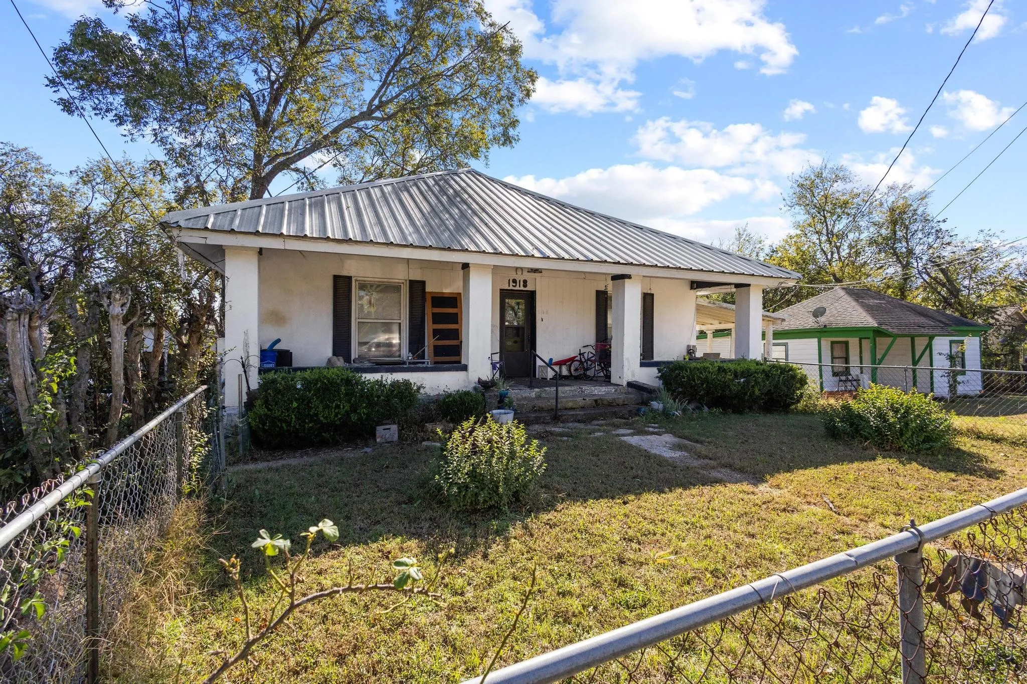White exterior with a metal roof, front porch, and mature landscaping