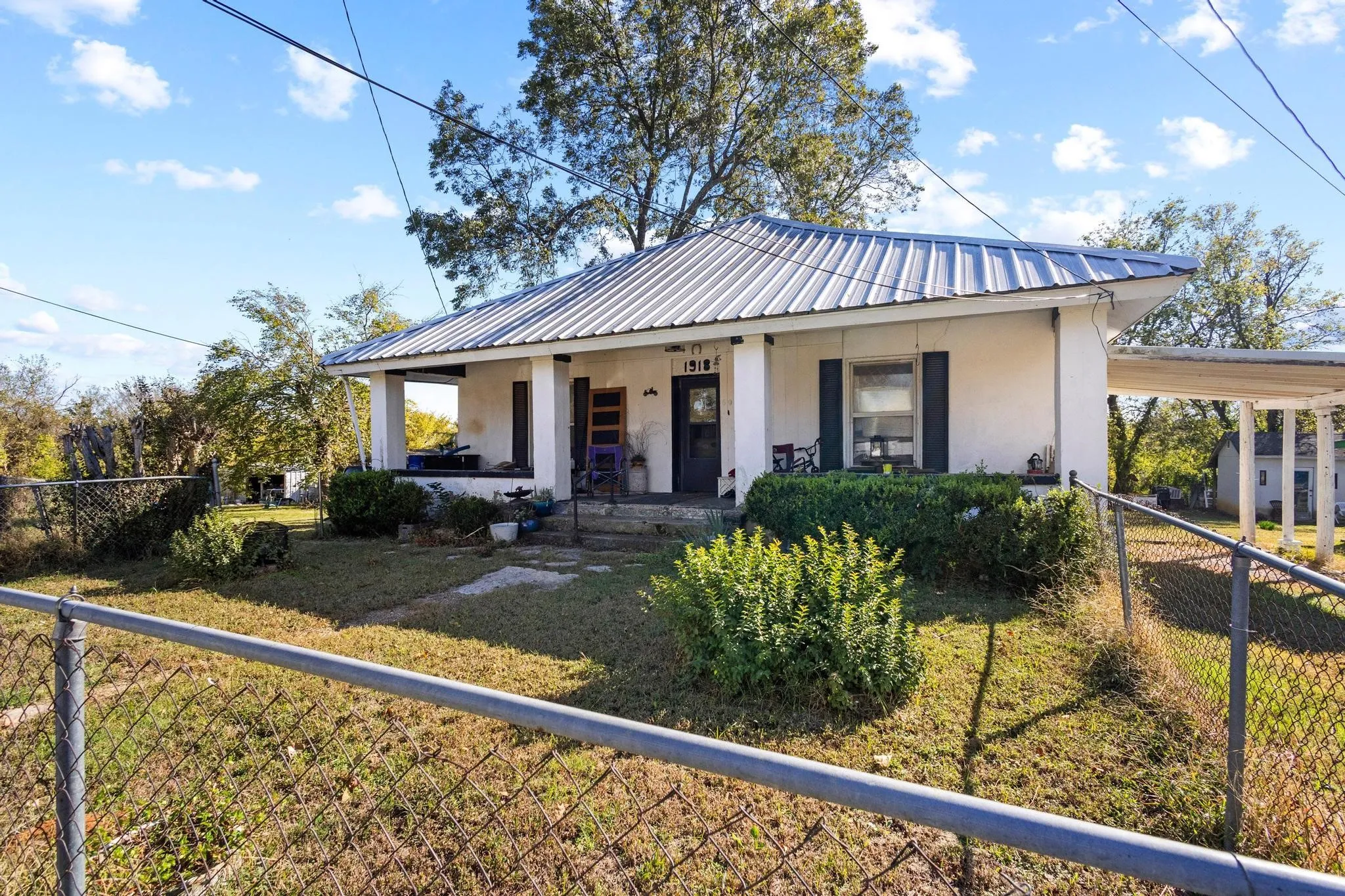 White exterior with a metal roof, covered front porch, and an attached carport