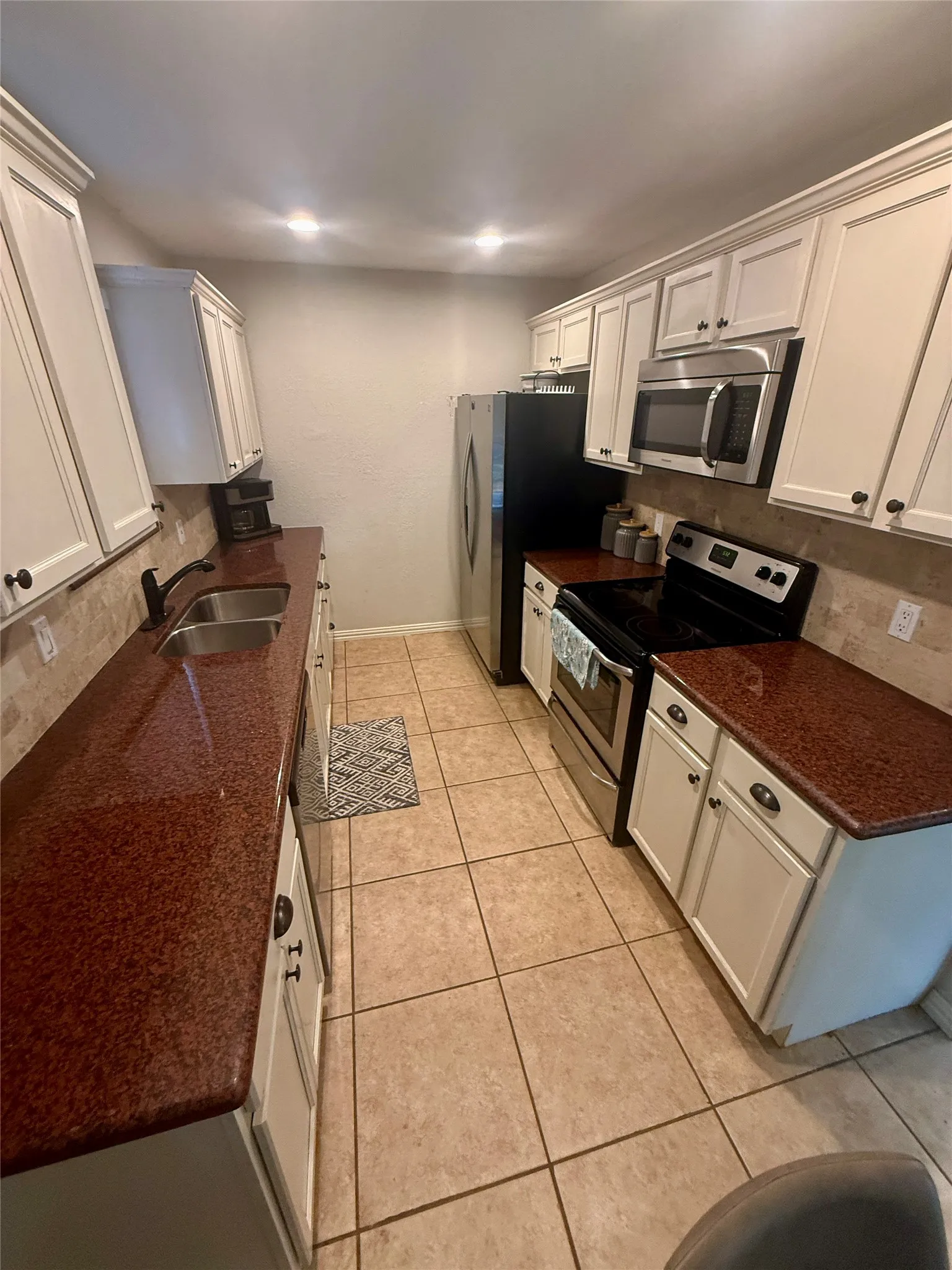 White shaker-style cabinetry with dark hardware, stainless steel appliances, speckled countertops, tile flooring, and recessed lighting