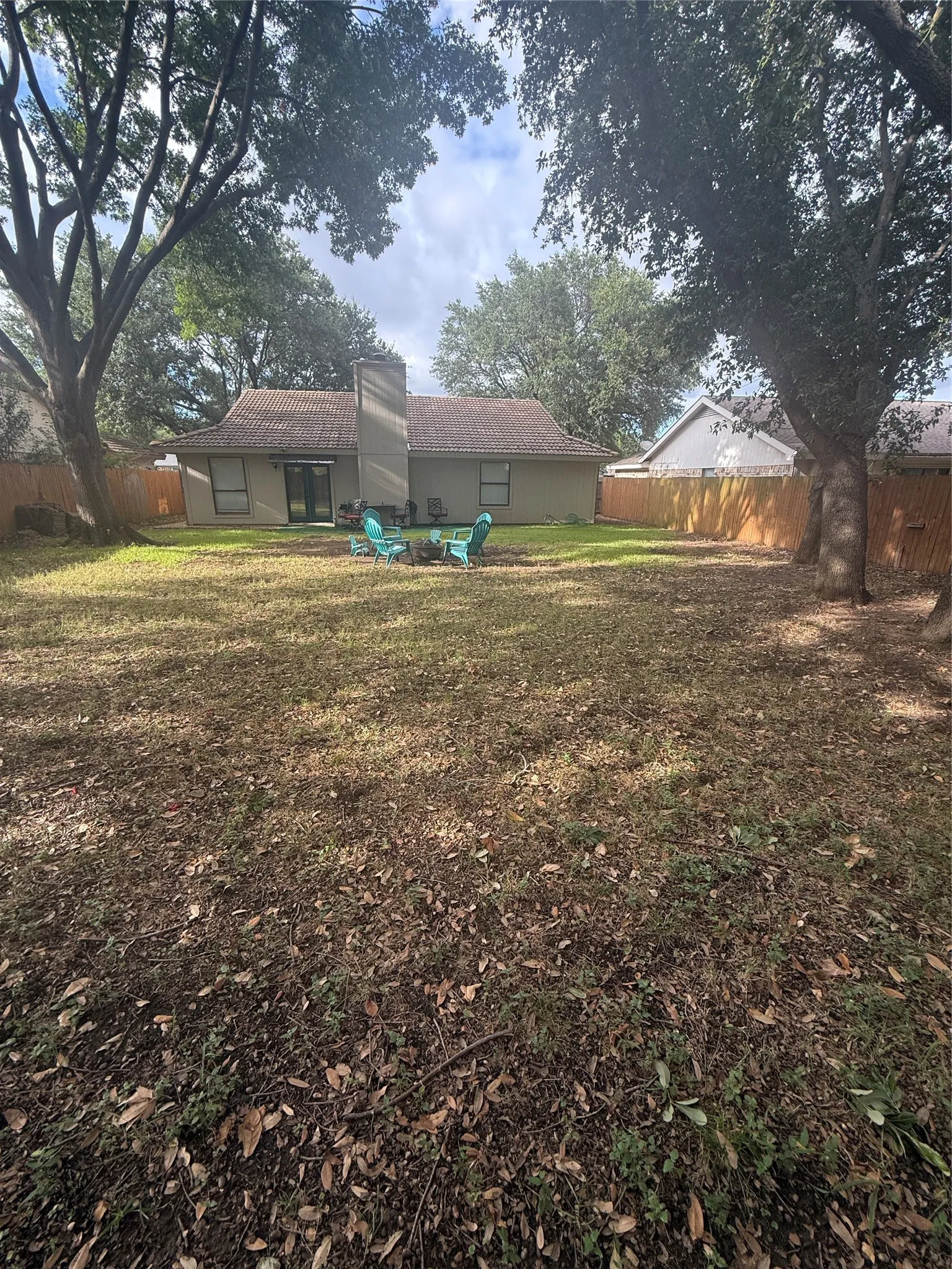 Expansive backyard featuring a privacy fence, mature trees, and a stucco exterior with a prominent chimney