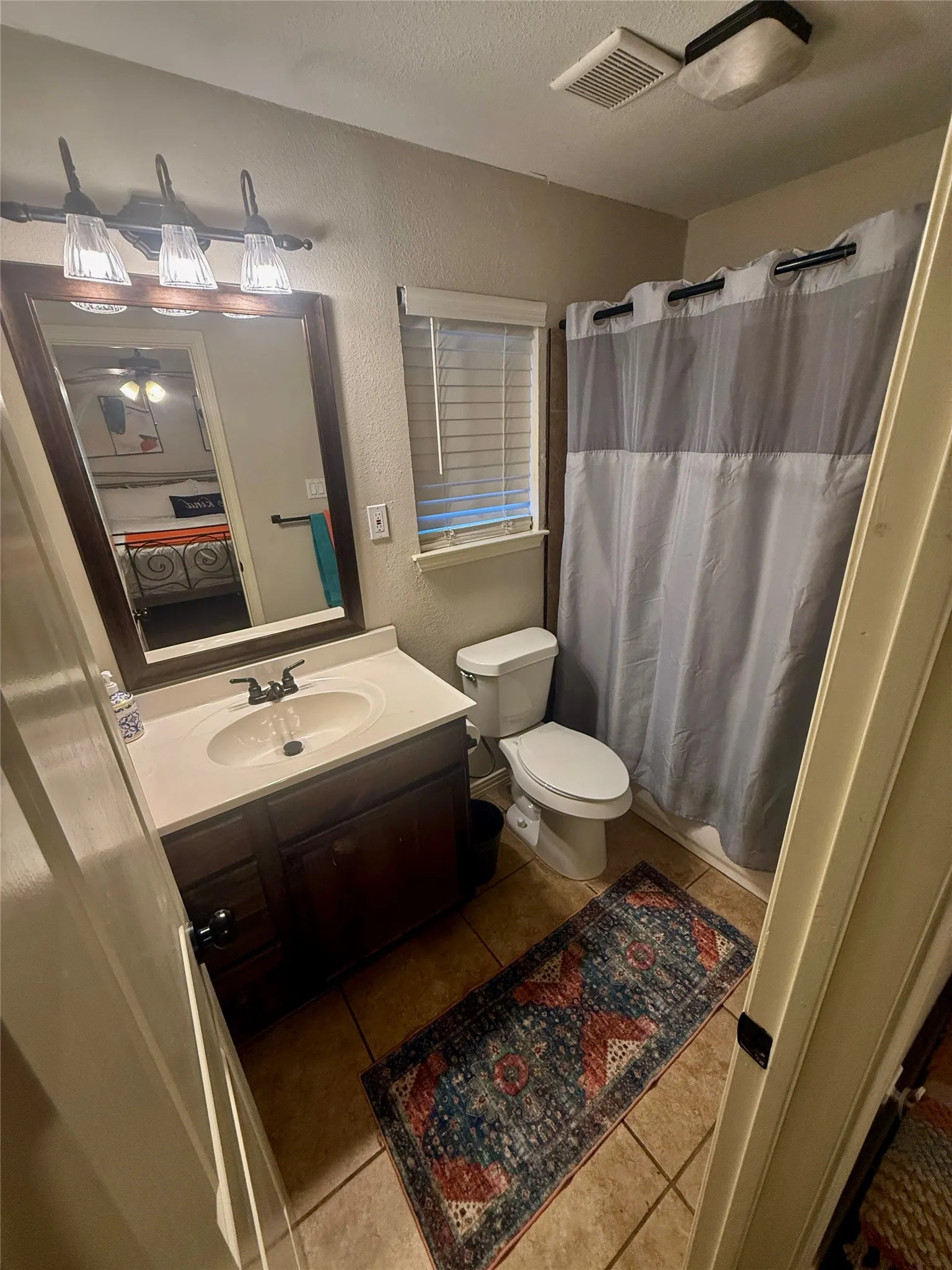 Bathroom featuring a dark wood-finish vanity with an integrated sink, a rectangular framed mirror, three-light vanity fixture, and a window with blinds