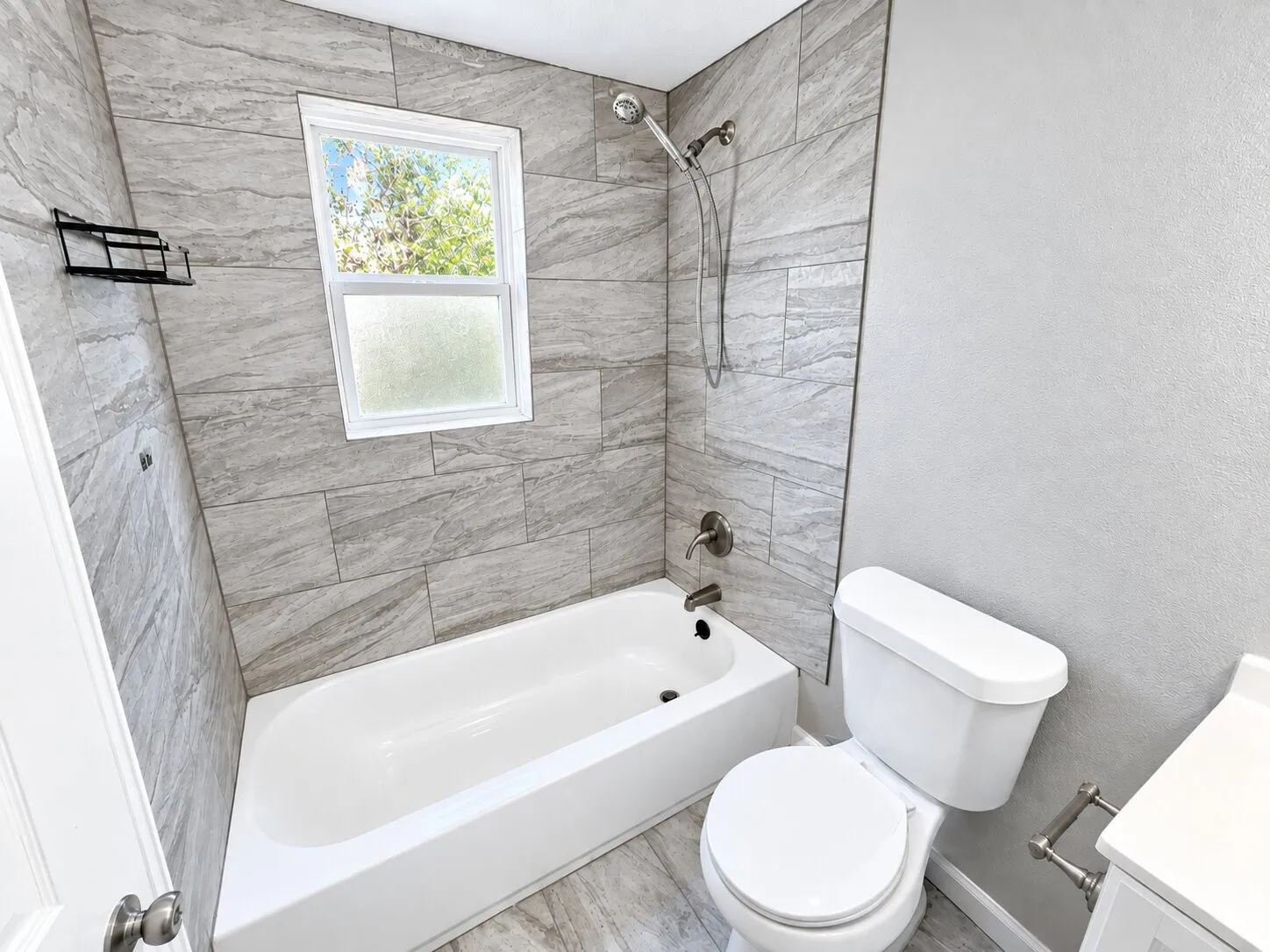 Bathtub with a shower fixture, tile surround, and a white framed window