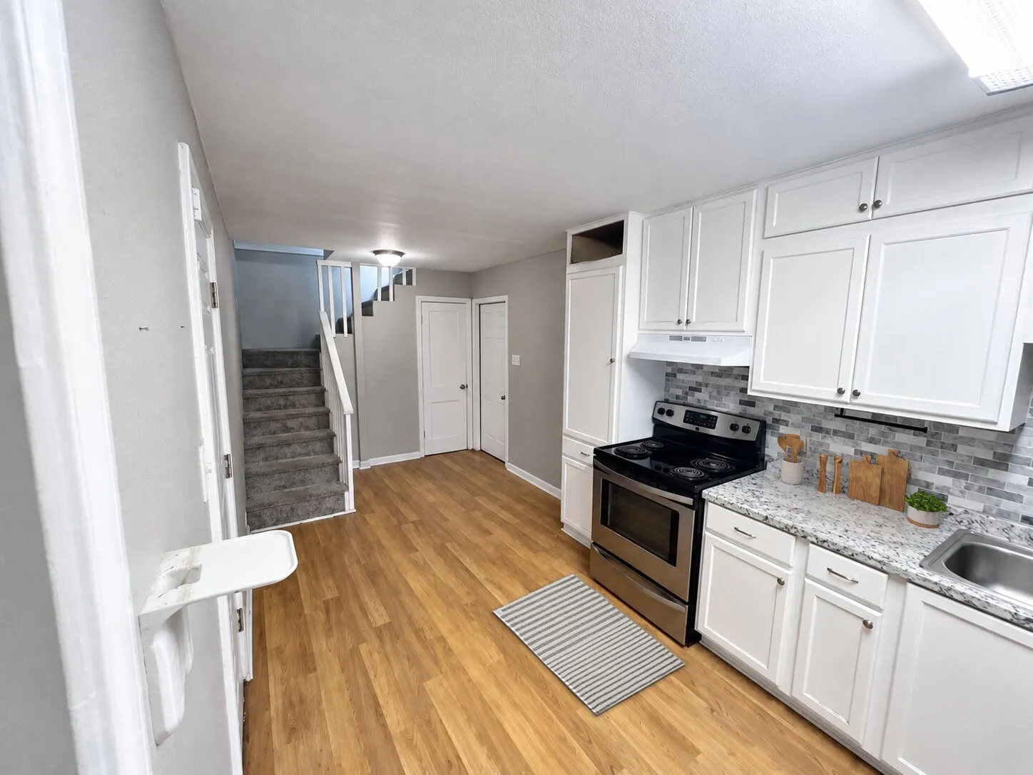 Kitchen featuring wood-finish flooring, white cabinetry, stainless steel range, and stone countertops with a tile backsplash