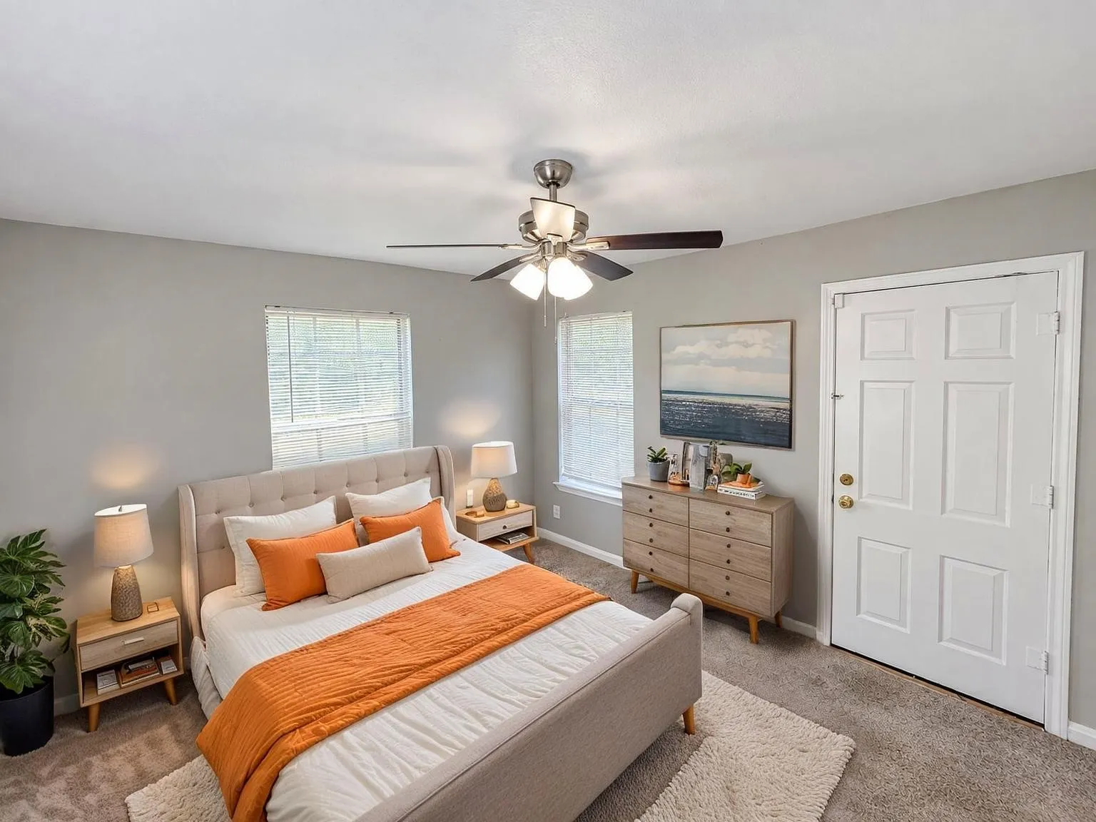 Virtually staged -
Carpeted room featuring a ceiling fan, two windows with blinds, a paneled door with brass hardware, and light gray wall paint