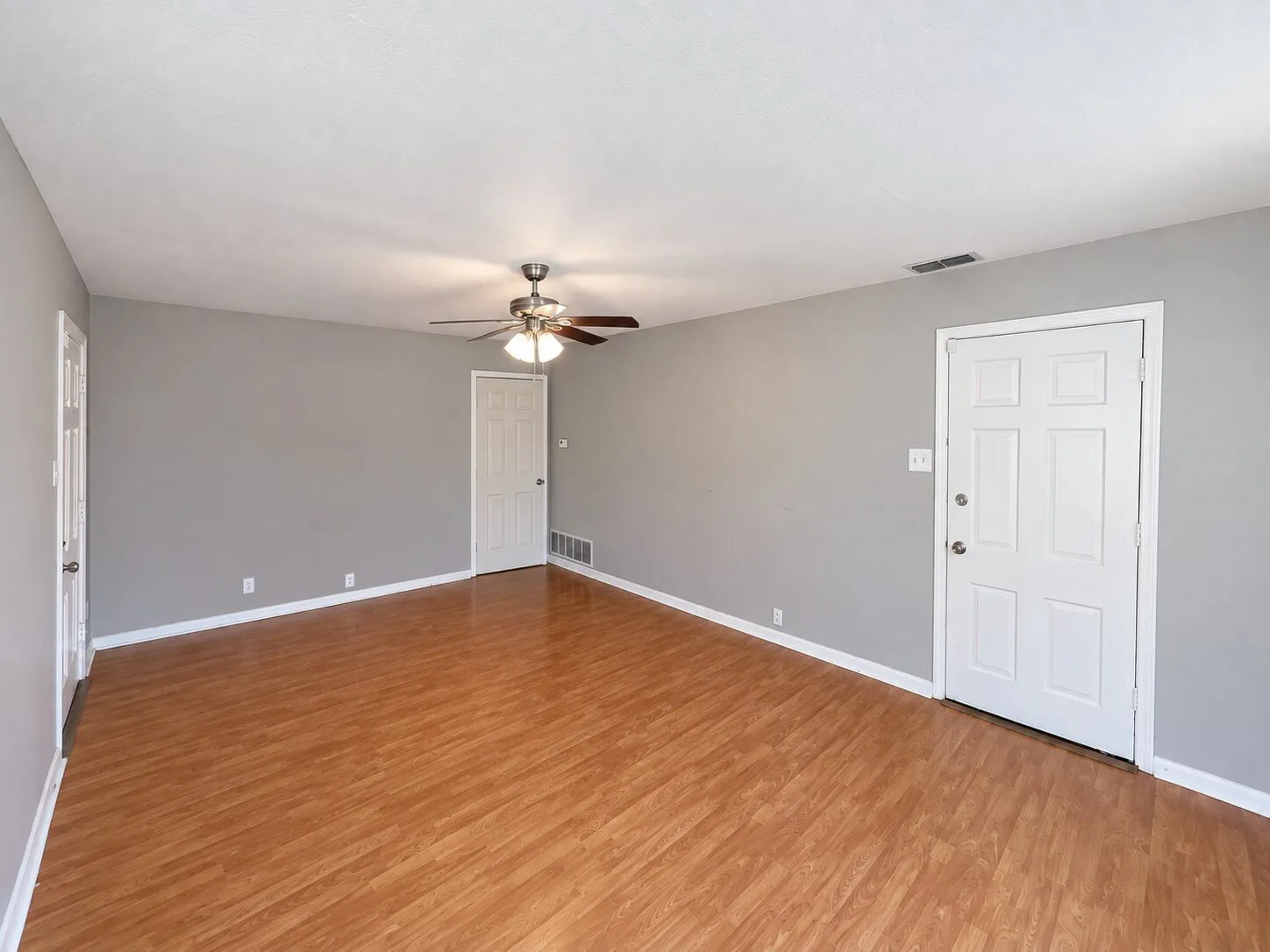 Wood-finish flooring throughout, neutral gray wall tones, ceiling fan with integrated lighting, and white paneled doors