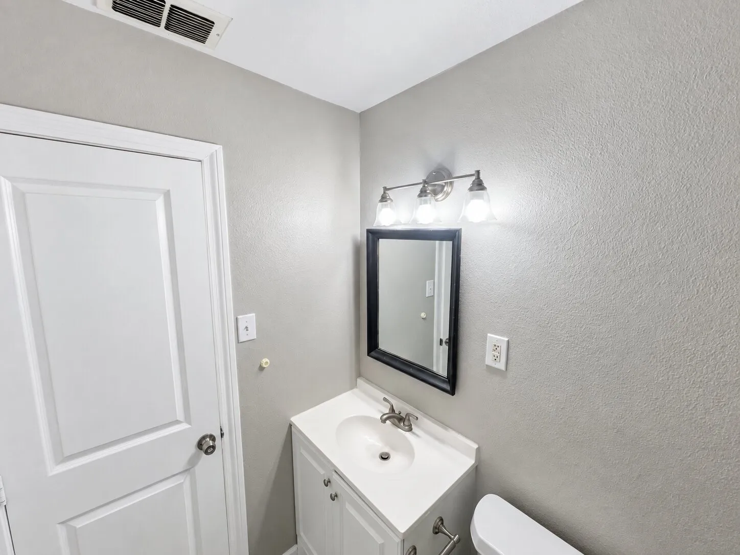White vanity with integrated sink, brushed nickel faucet, framed mirror, and brushed nickel light fixture