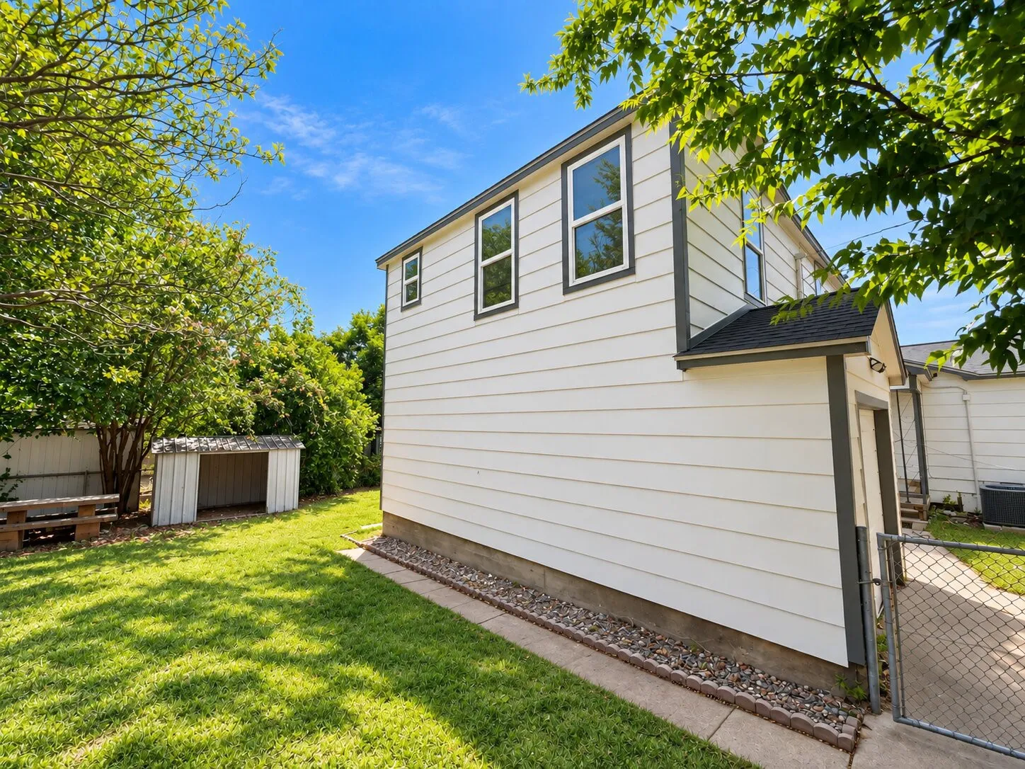 Expansive side yard featuring a manicured lawn, established landscaping, and a detached shed