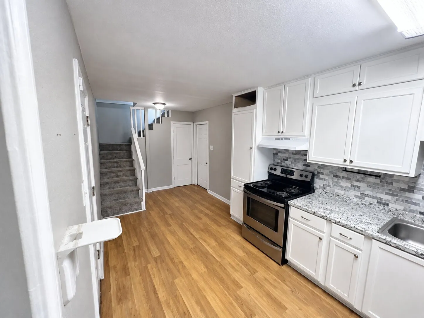 Kitchen featuring white cabinetry, stainless steel range, light-toned wood-finish flooring, and a mosaic tile backsplash