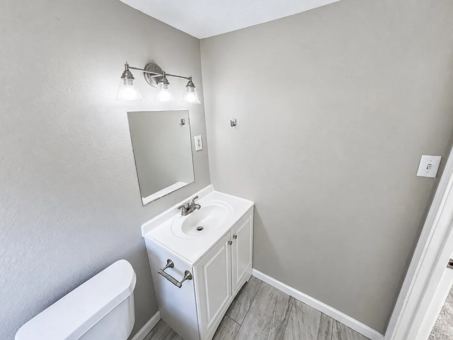 White vanity with integrated sink, brushed nickel faucet, mirror, and coordinating vanity light fixture