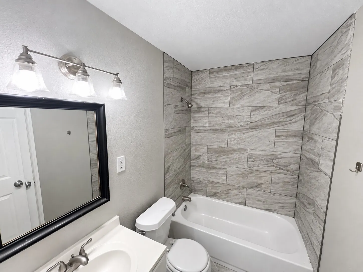 Bathroom featuring a vanity with an integrated sink, a framed mirror, a three-light fixture, and a bathtub with tiled surround