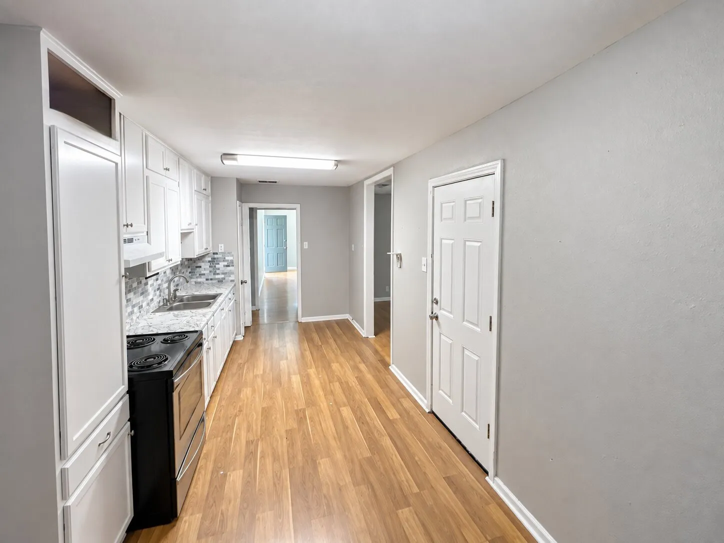 Galley kitchen featuring white cabinetry, stone-finish countertops, tile backsplash, and wood-finish flooring