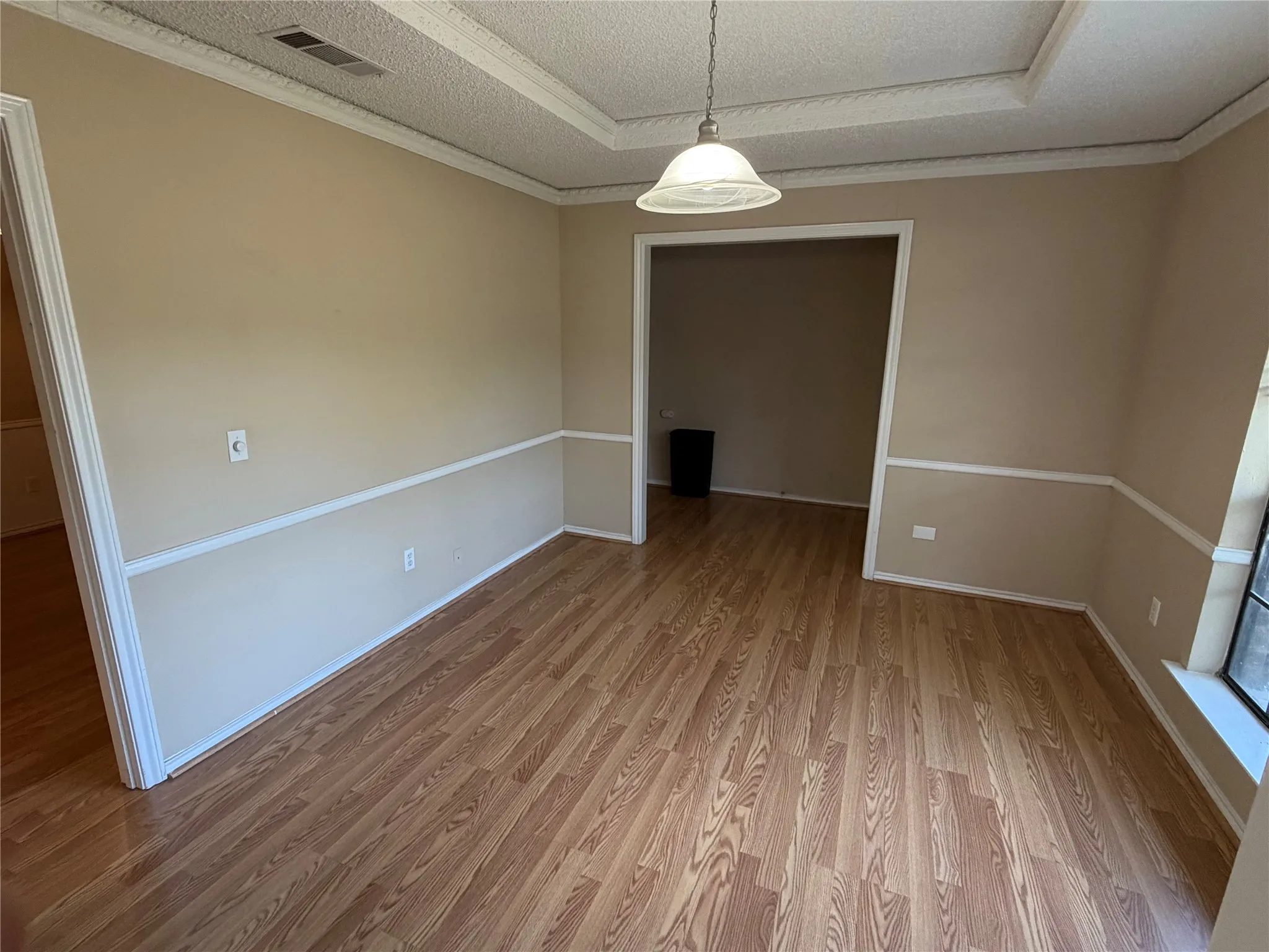 Wood-finish flooring, two-tone wall treatment with chair rail, recessed ceiling detail, and a white dome pendant light fixture
