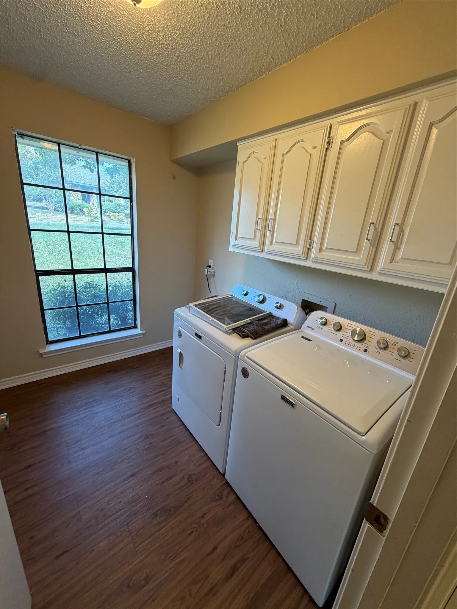 Wood-finish flooring, overhead cabinetry, and a window with exterior views