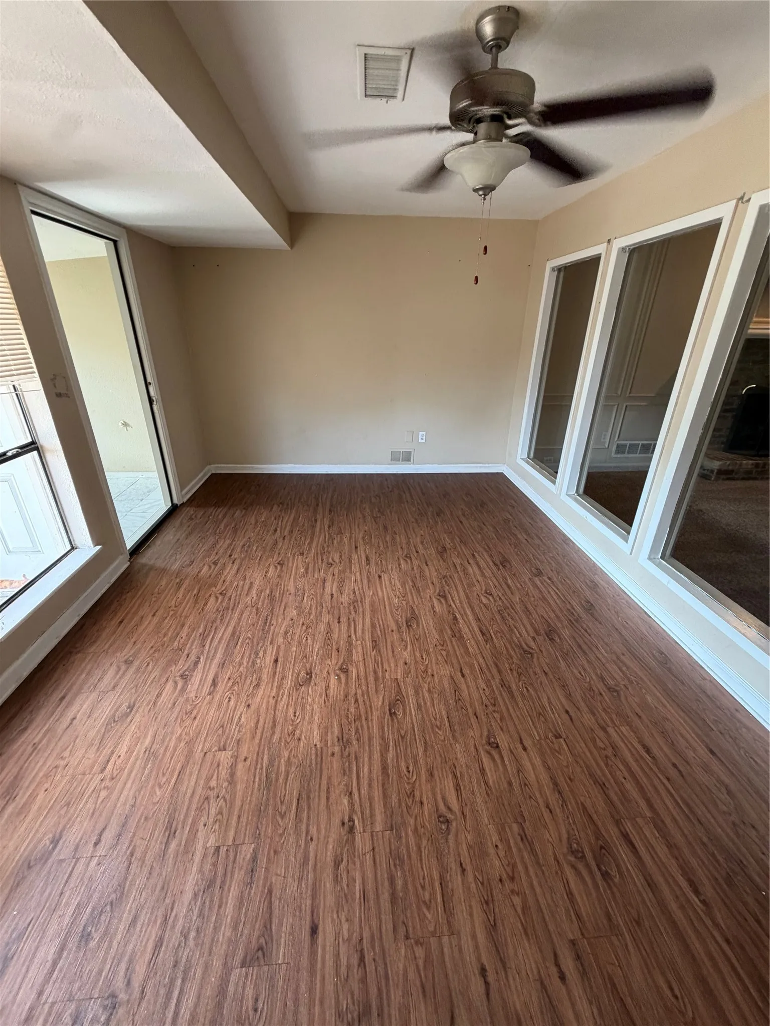 Wood-finish flooring with perimeter baseboards, multiple windows, and a ceiling fan with integrated lighting