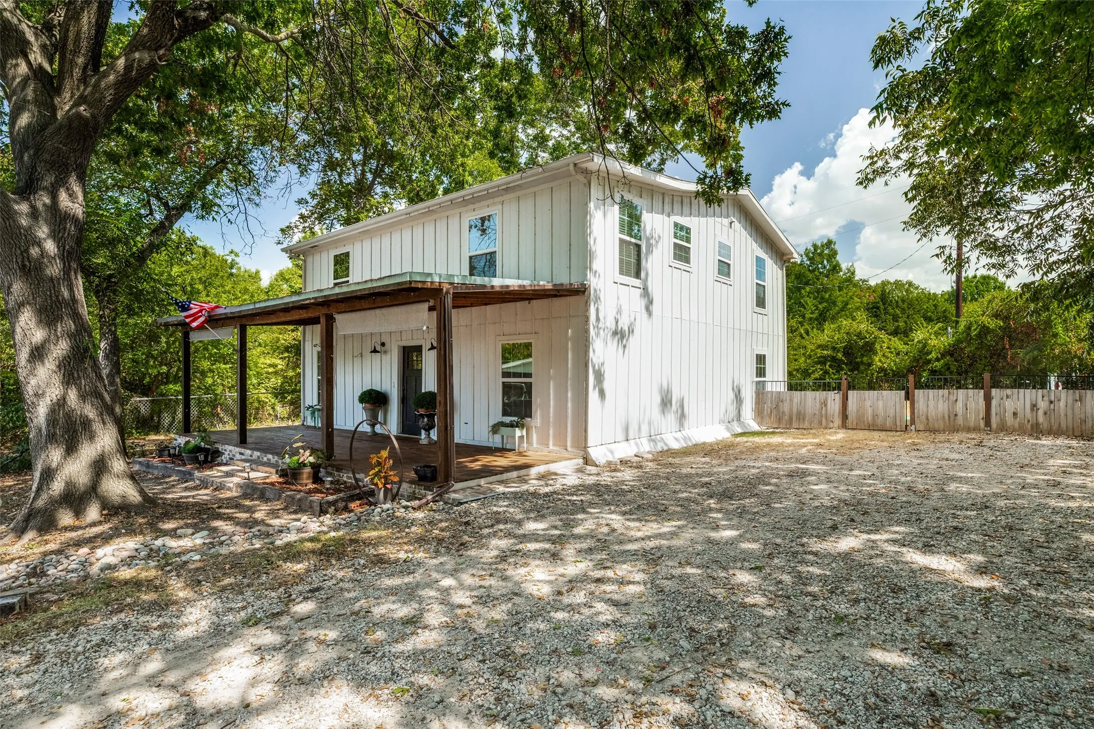 White board and batten exterior, covered wooden porch, gravel parking area, and a wooden privacy fence